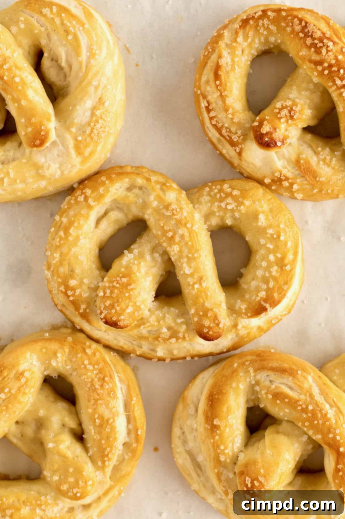 A close-up view of five perfectly shaped homemade soft pretzels resting on a sheet of parchment paper, beautifully golden and ready for baking.