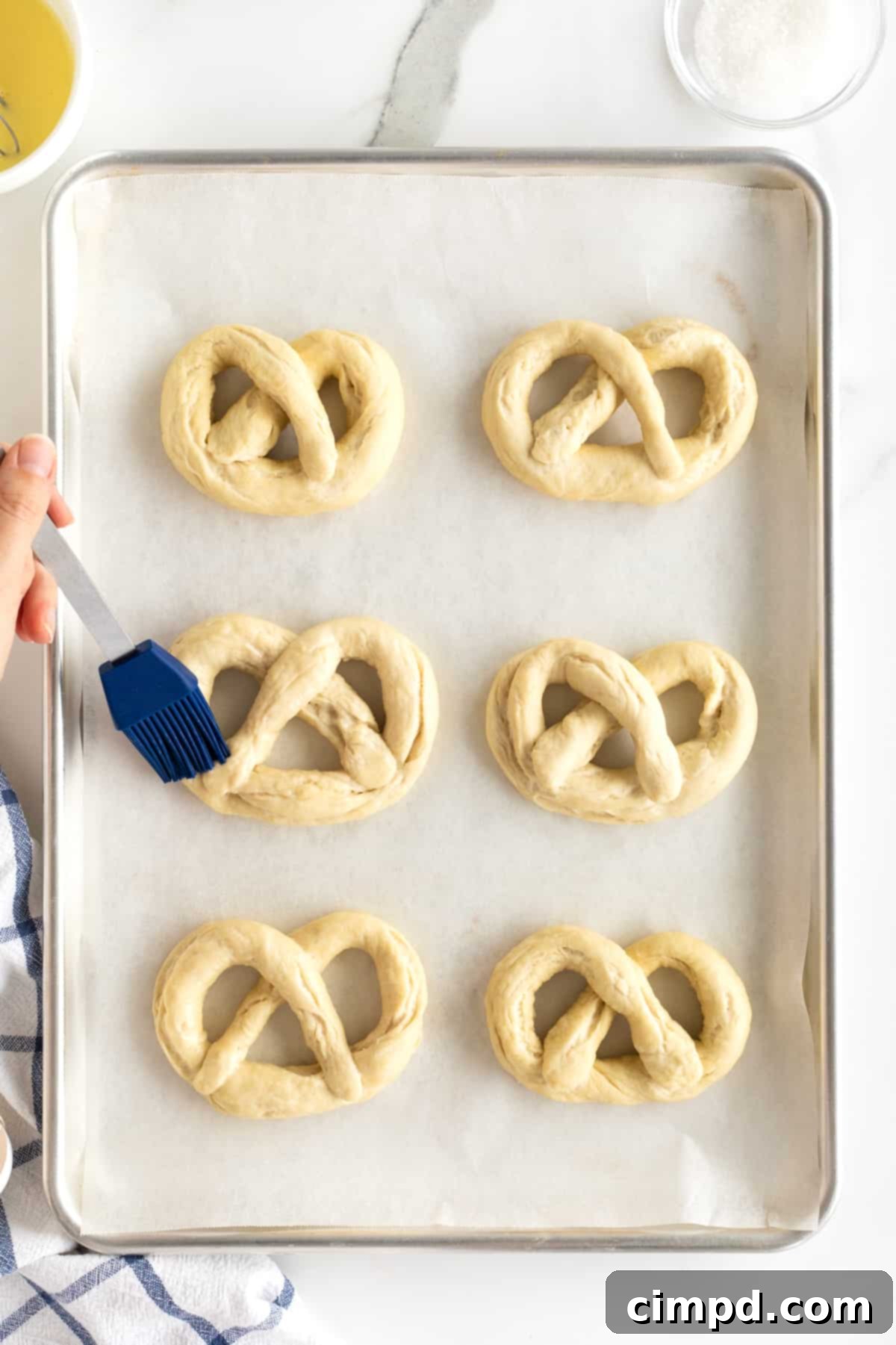 Six uncooked soft pretzels, freshly brushed with egg wash and generously sprinkled with coarse salt, arranged on a parchment-lined baking sheet.