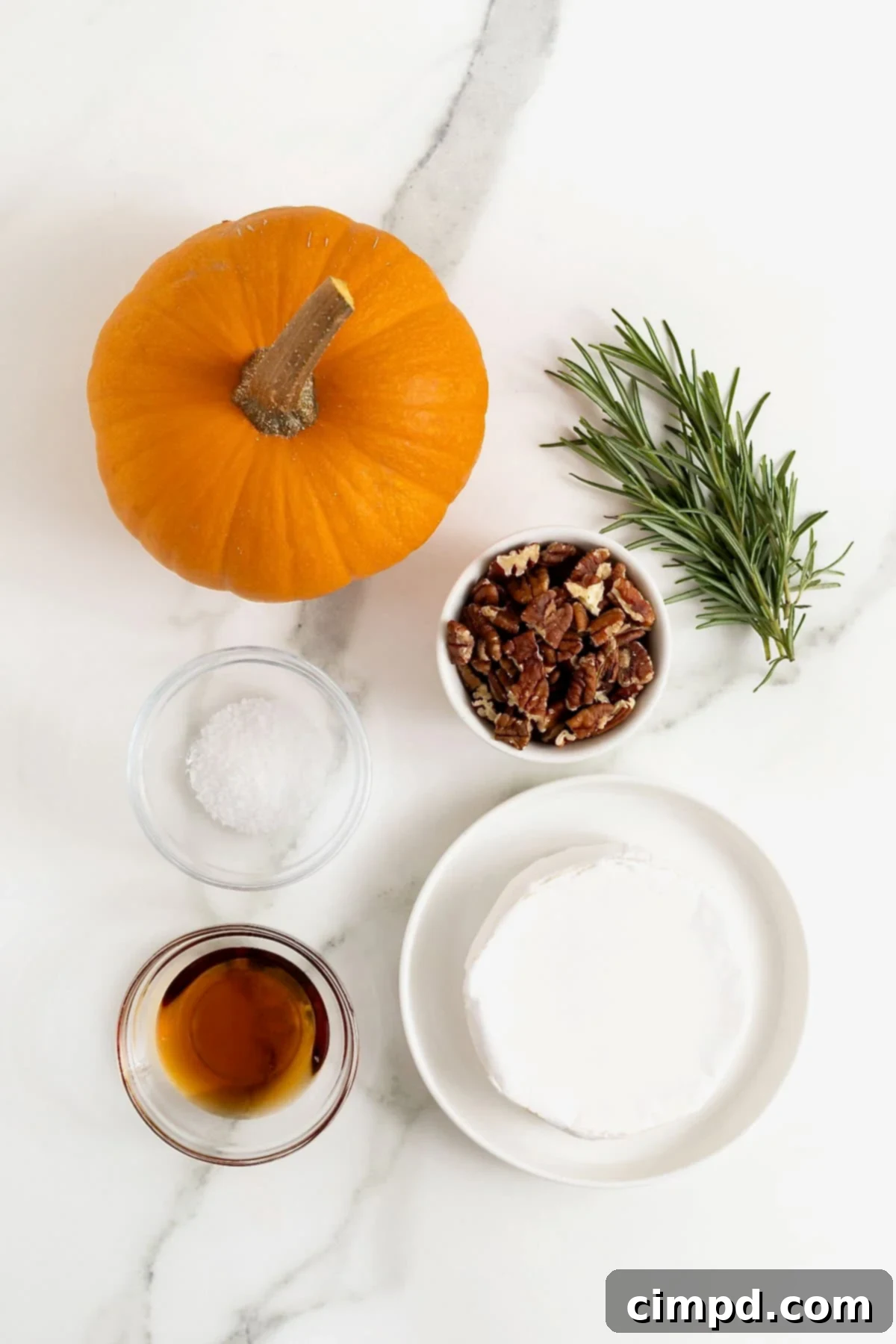 All the fresh ingredients laid out on a white marble counter, ready to be transformed into a delicious pumpkin baked brie with maple, pecans, and rosemary.