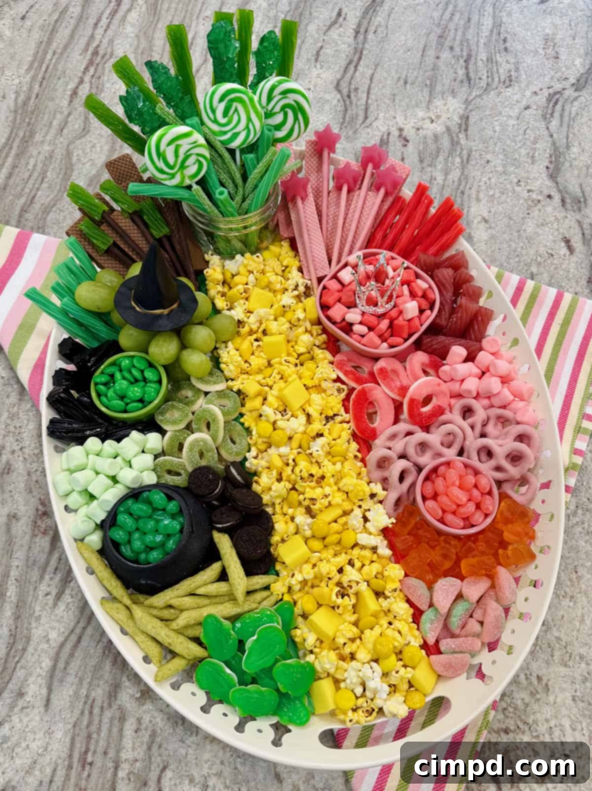 A beautifully arranged Wicked Movie Snack Board, divided into pink and green sections, with a yellow brick road centerpiece, on a gray marble counter.