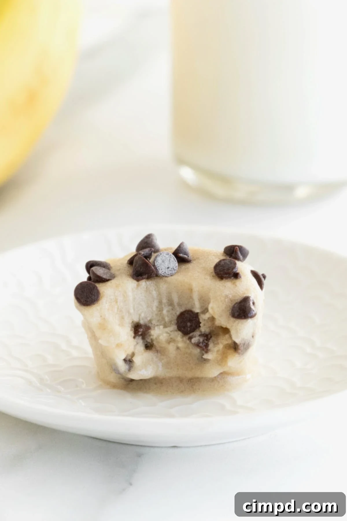 A single, perfectly portioned chocolate chip banana ice cream bite on a small white plate, with a small bite taken out, revealing its creamy interior.