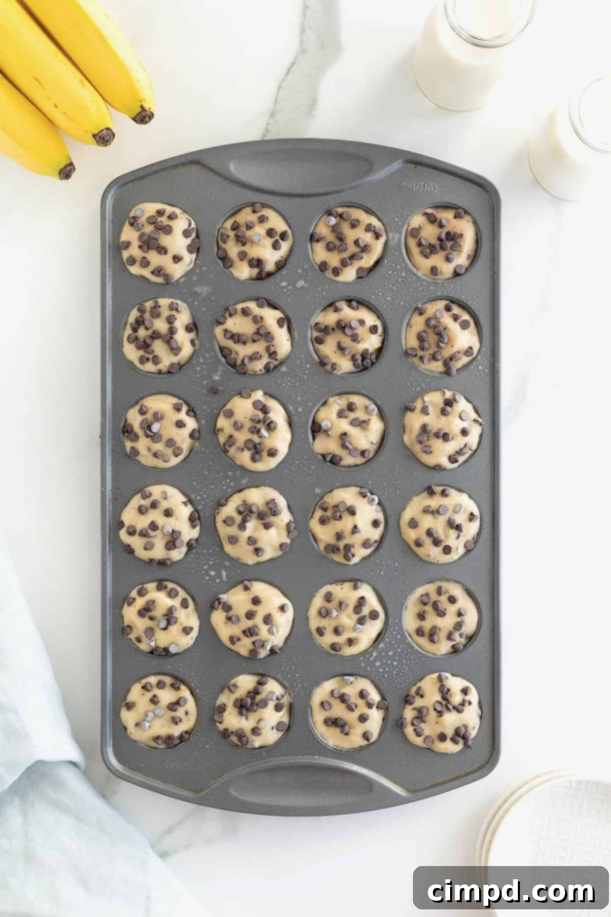 Two-Ingredient Banana Chocolate Chip Ice Cream Bites nestled in an aluminum mini muffin pan, resting on a sophisticated white marble counter.