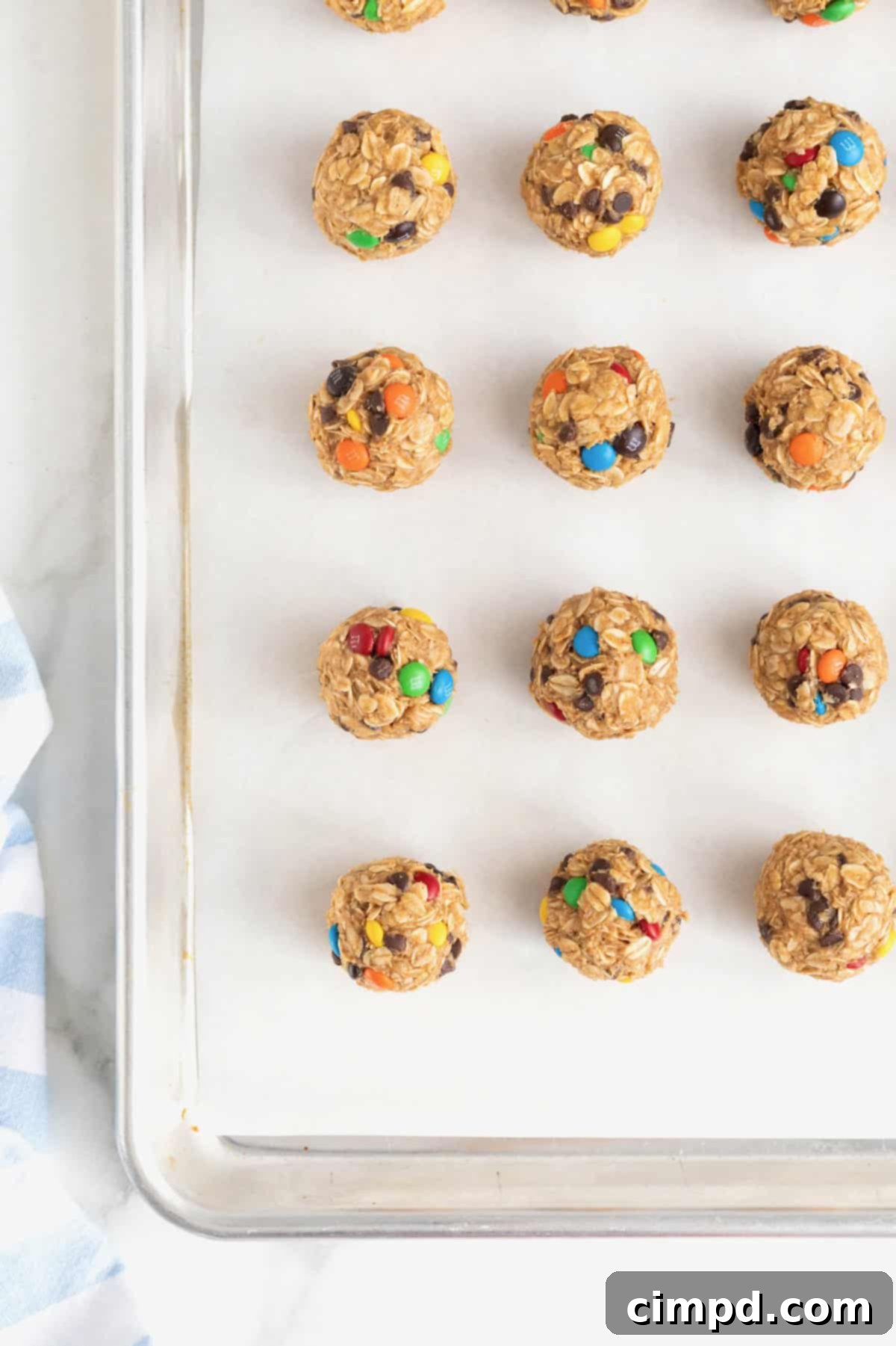 No-Bake Monster Cookie Bites 11 A baker's dozen of no-bake cookie balls, featuring a colorful mix of mini M&Ms, neatly arrayed on a parchment-lined baking sheet.