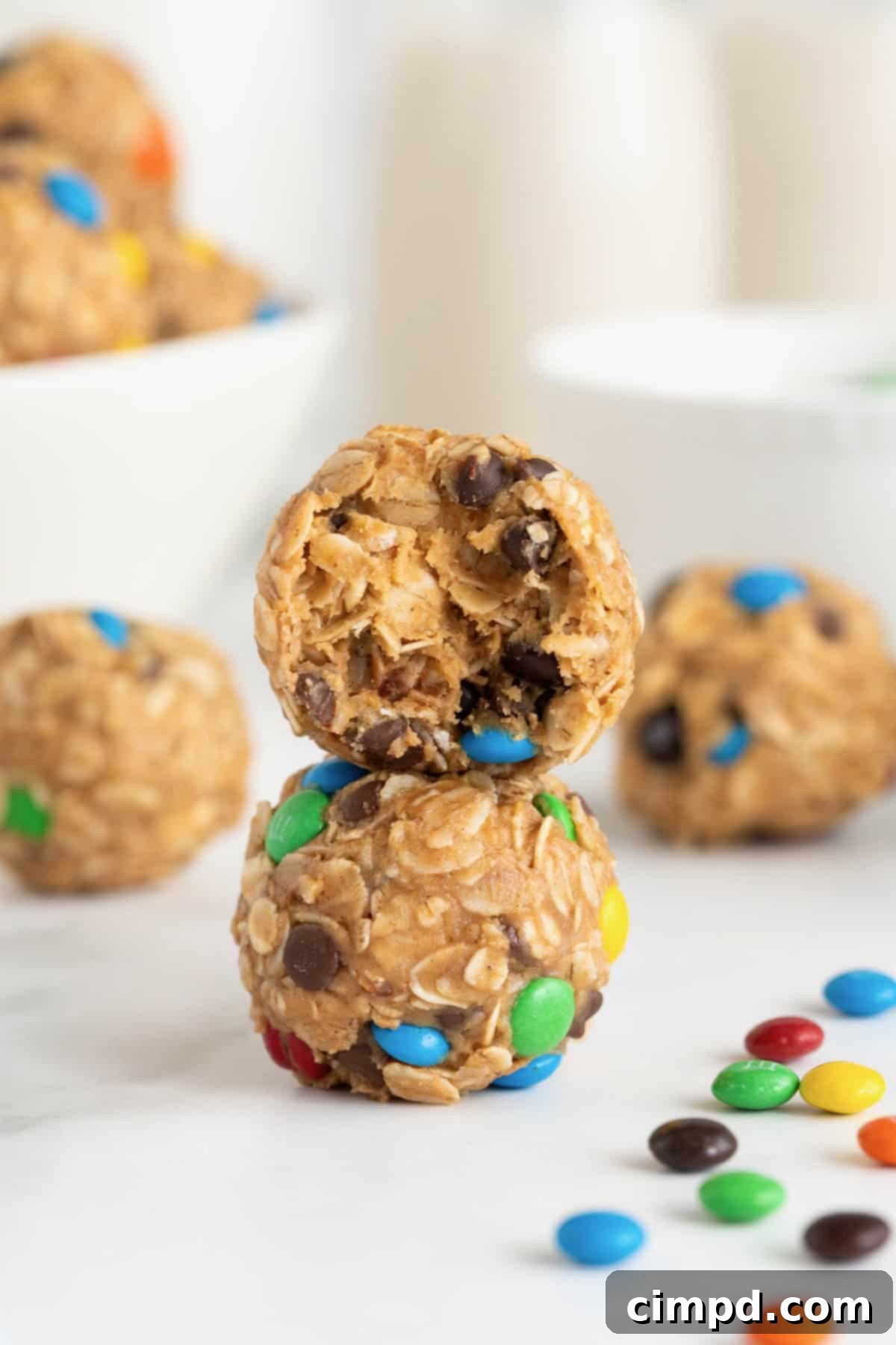No-Bake Monster Cookie Bites 3 Two perfectly rounded monster cookie balls, one with a small bite taken out, stacked elegantly on a clean white marble countertop.