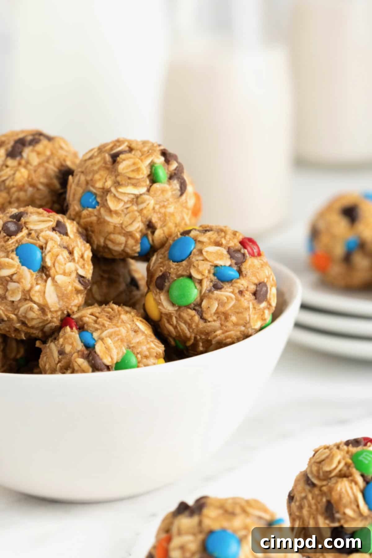 No-Bake Monster Cookie Bites 6 A charming white bowl brimming with colorful no-bake monster cookie balls, set against a pristine white marble counter.