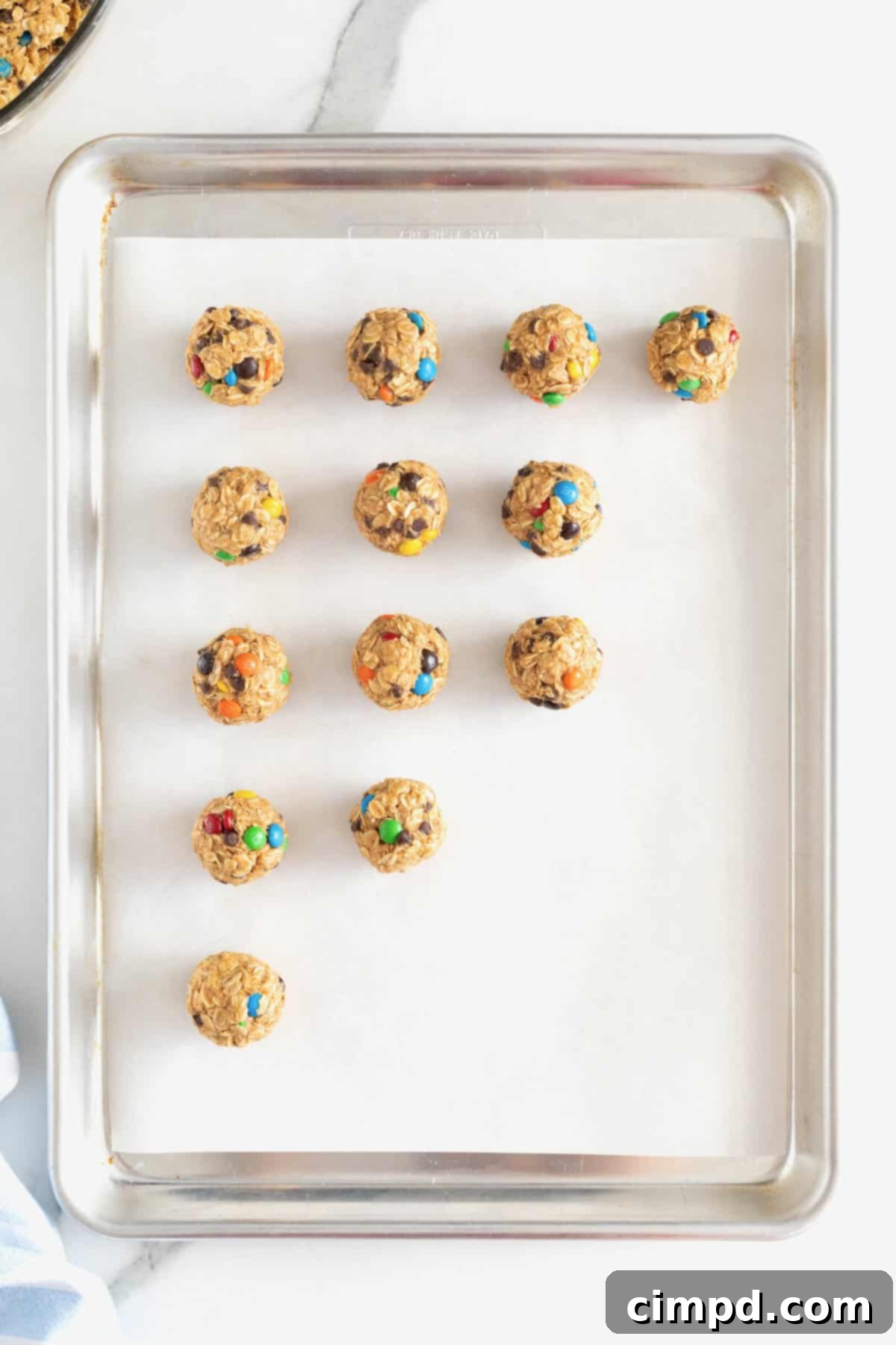 No-Bake Monster Cookie Bites 9 A beautifully arranged selection of 13 no-bake cookie balls, adorned with colorful mini M&Ms and mini chocolate chips, on a parchment-lined aluminum baking tray.