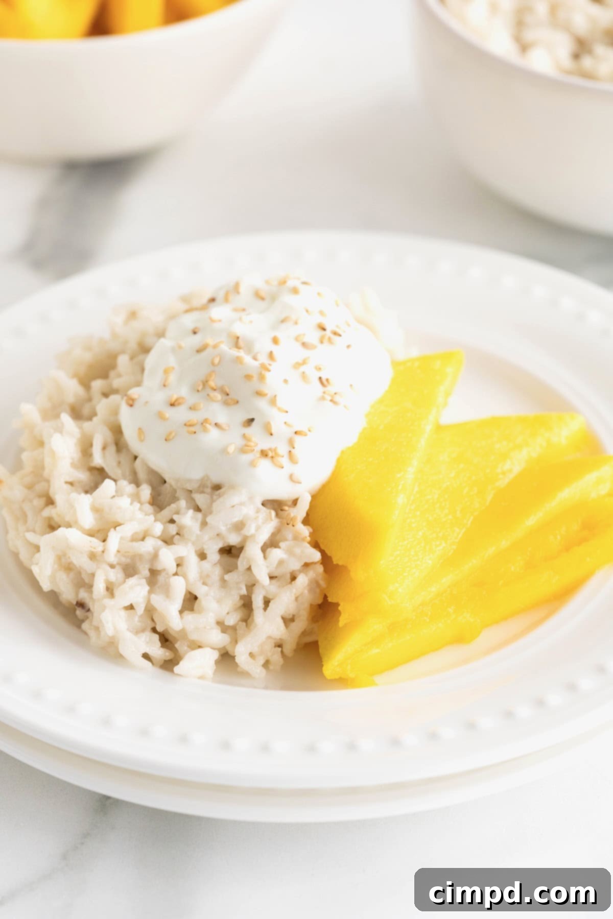 A close-up shot of a small white plate of mango sticky rice on a clean white marble counter, ready to be enjoyed.