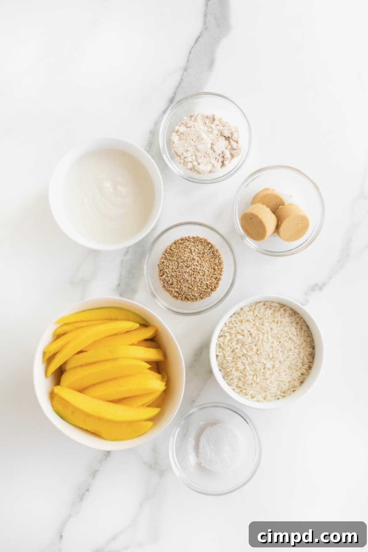 A collection of ingredients necessary to make Thai mango sticky rice, neatly arranged in small glass dishes on a white marble counter.