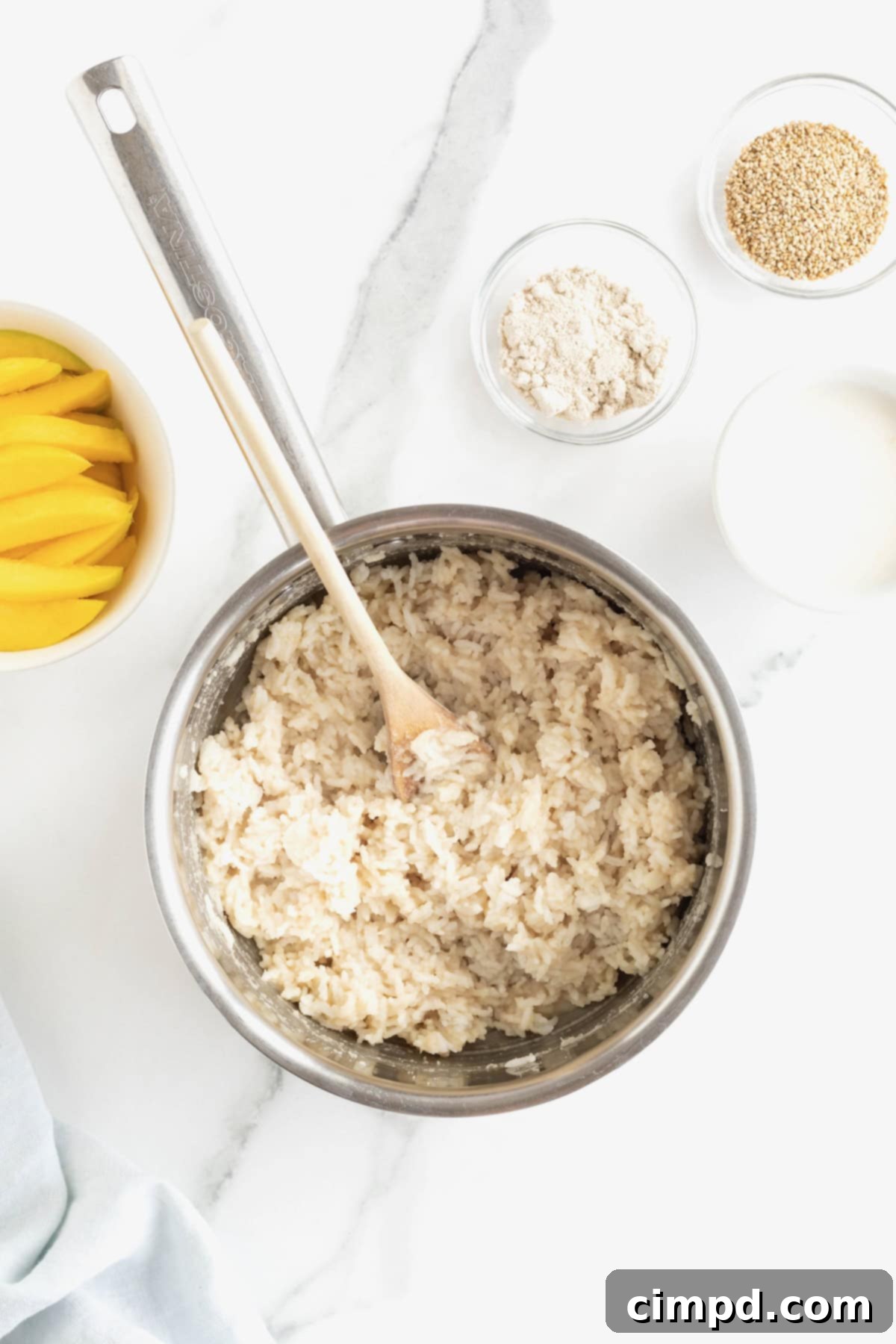 A saucepan filled with sticky rice, with a wooden spoon resting inside, after it has absorbed the coconut cream.