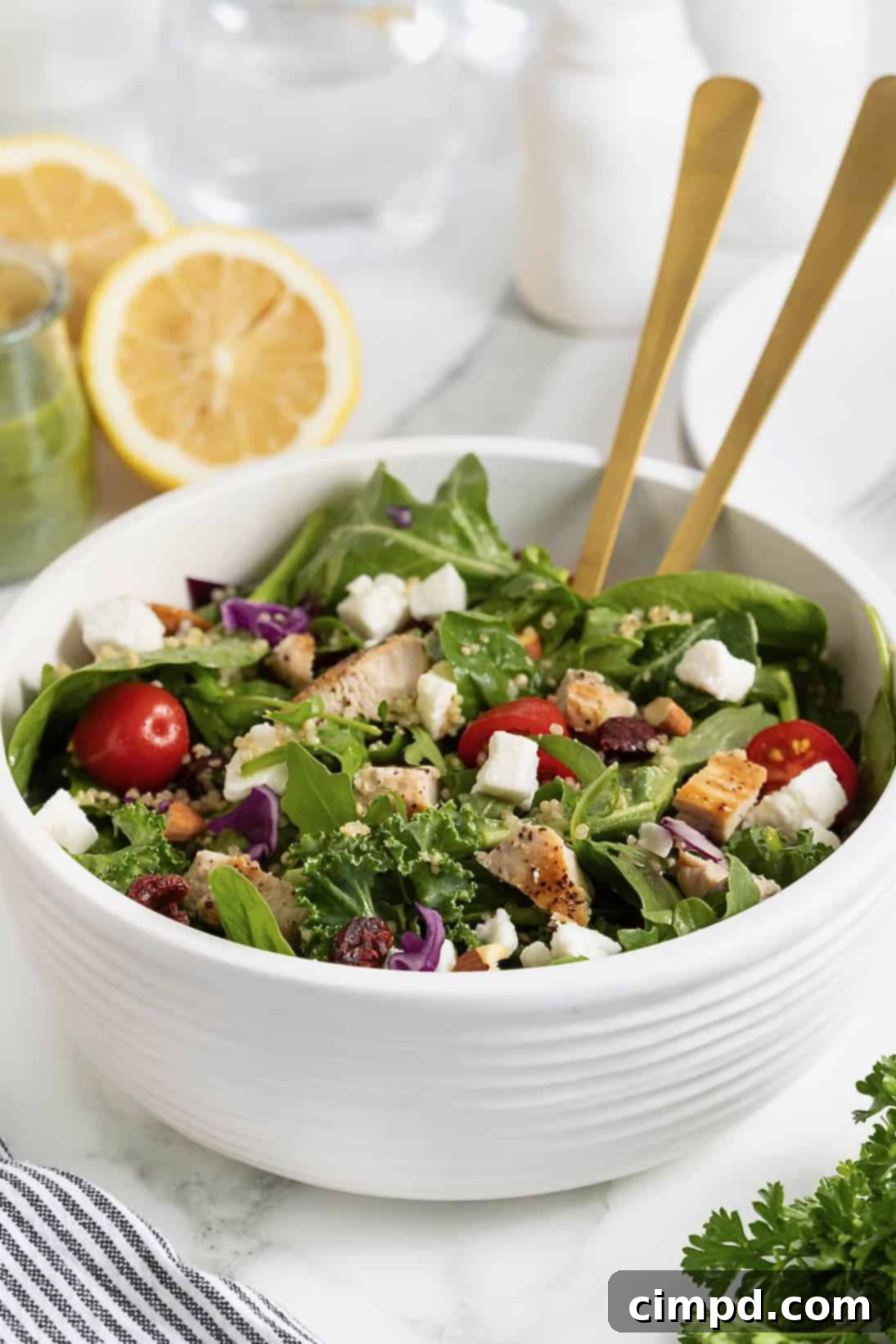 A vibrant green salad with cherry tomatoes, crumbled feta cheese, and fluffy quinoa in a large white serving bowl, featuring two elegant wooden spoon handles.