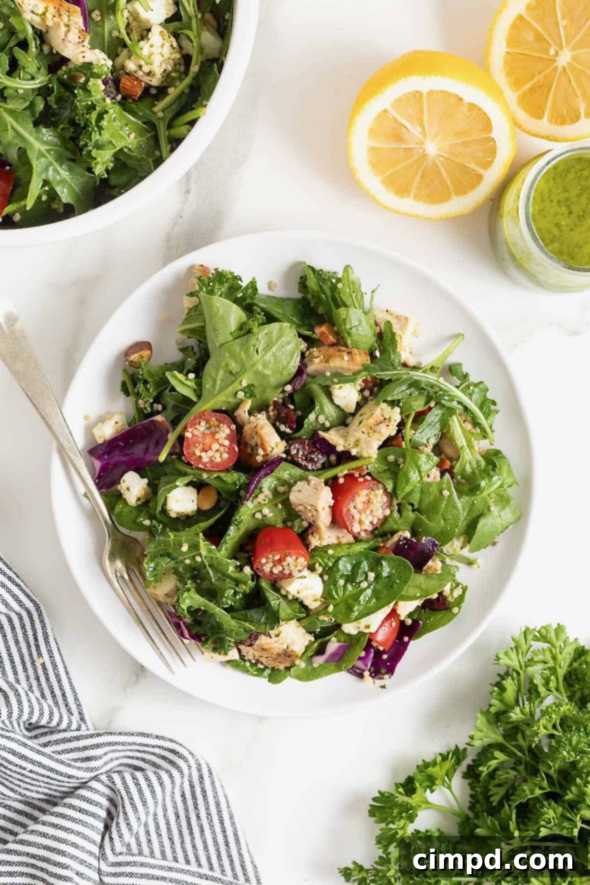 A close-up view of a plate featuring a portion of green salad with halved cherry tomatoes, cooked quinoa, and tender chicken pieces.