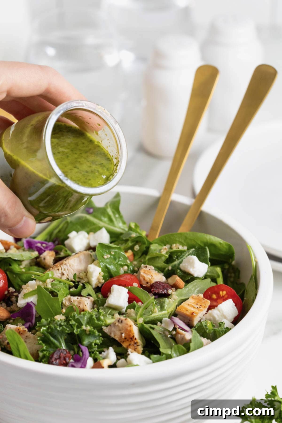 A small glass carafe gently pouring vibrant green salad dressing over a fresh green salad nestled in a large white bowl.