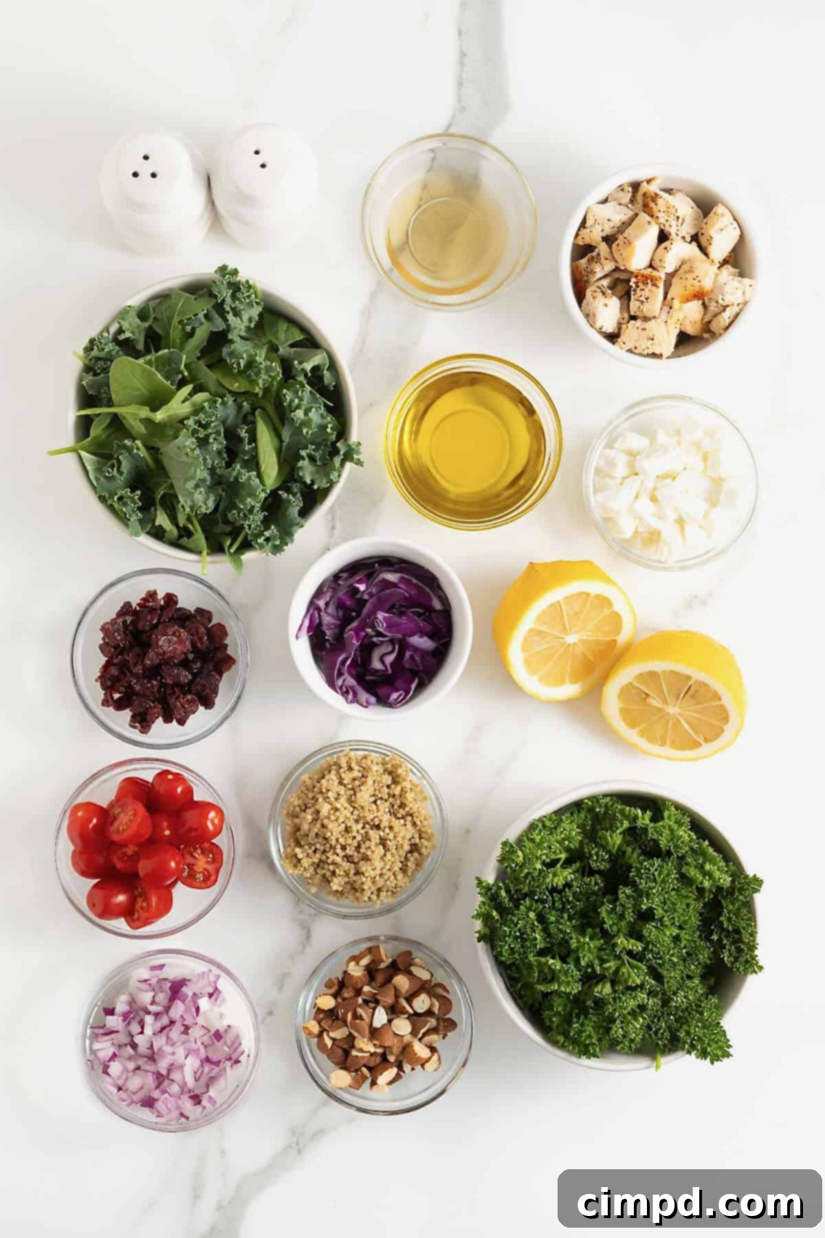 Various fresh ingredients for making a chicken quinoa salad, neatly arranged in small clear glass dishes on a pristine white marble counter.