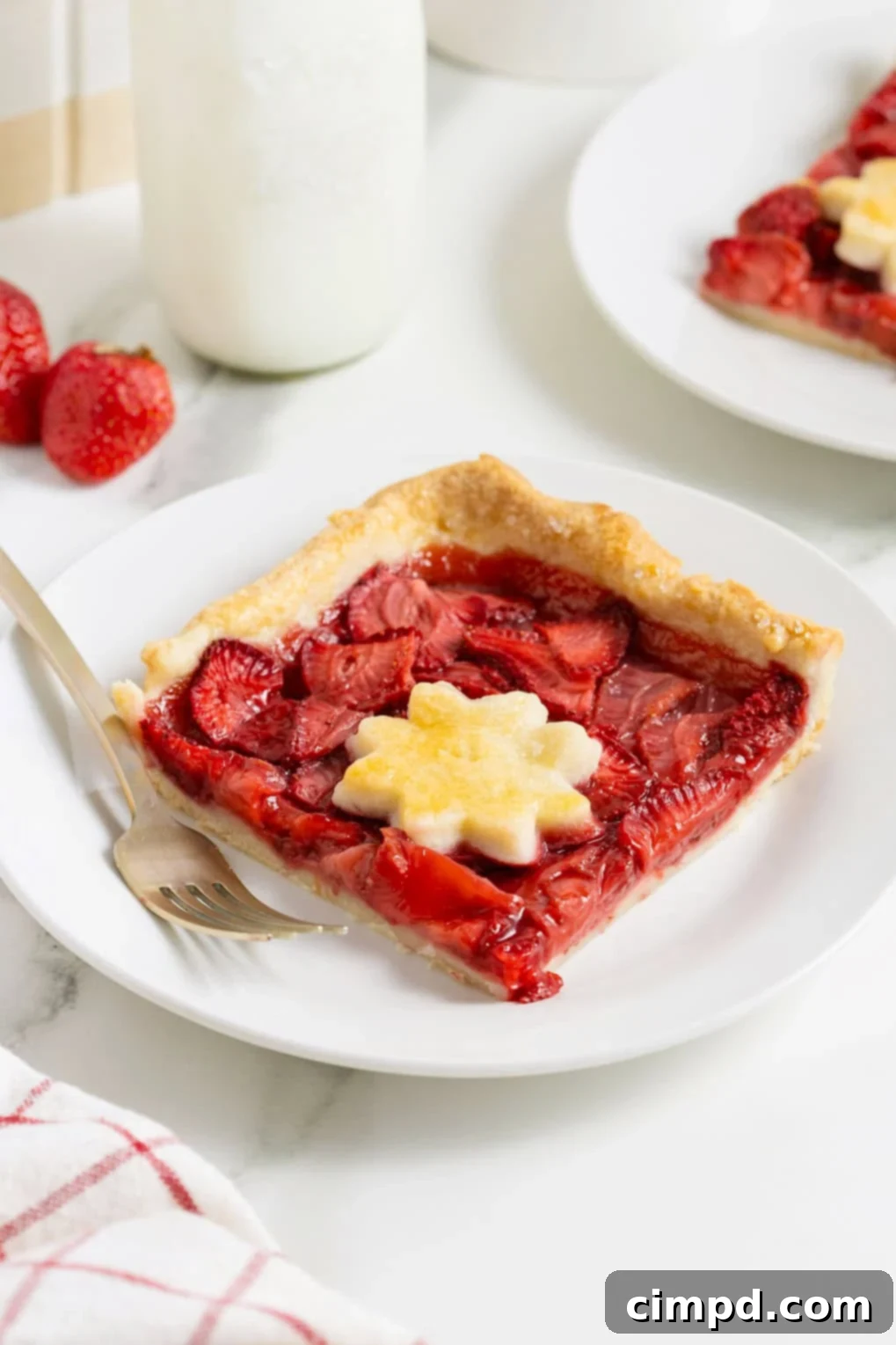 Summer Strawberry Slab Pie 3 A perfectly golden slice of Strawberry Slab Pie, showcasing its rich, ruby-red filling and flaky crust, rests on a small white plate with a gold-toned fork, ready to be enjoyed.