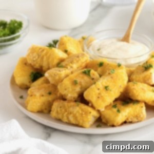 Crispy Baked Fish Fingers 14 A large white serving plate with a pile of golden battered fish sticks surrounding a small glass dish of tartar sauce.
