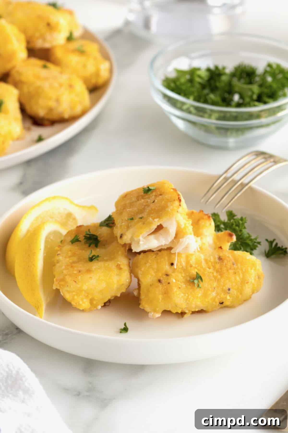 Crispy Baked Fish Fingers 3 A white plate featuring four perfectly golden baked fish sticks, garnished with two fresh lemon slices.