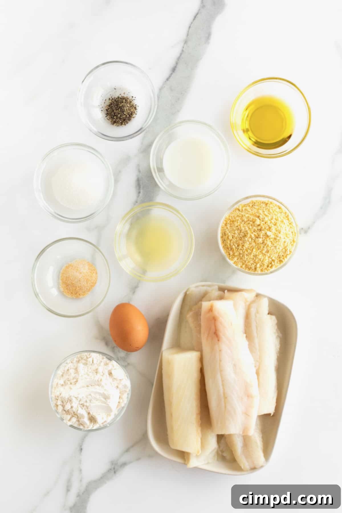 Crispy Baked Fish Fingers 8 A beautifully arranged selection of ingredients for baked fish sticks, displayed in small glass dishes on a pristine white marble counter.