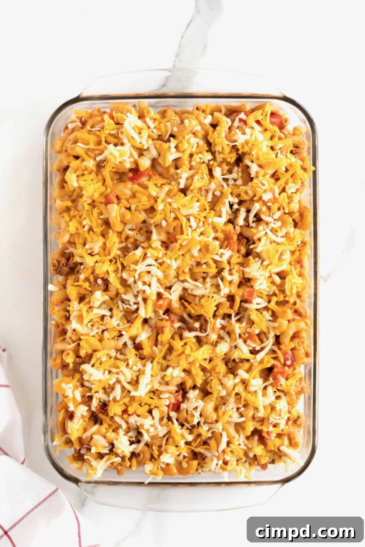 Fiesta Mac and Cheese 13 A 9x13 glass baking dish with Mexican macaroni casserole, topped with a generous sprinkle of Mexican blend shredded cheese, pre-baking.