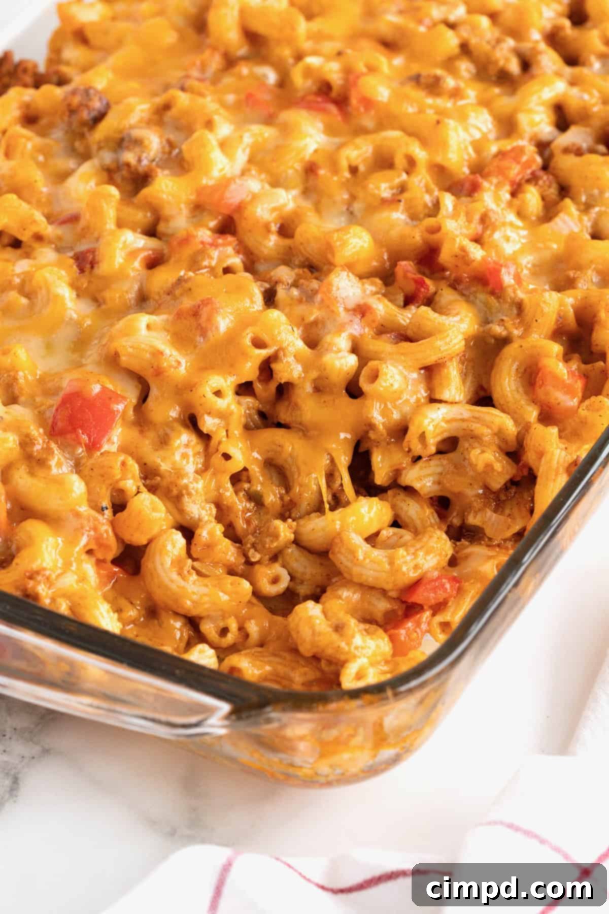 Fiesta Mac and Cheese 15 A close-up of a glass casserole dish filled with Mexi Mac and Cheese, showcasing the perfectly cooked elbow macaroni, chunks of red tomato, and a beautiful blend of melted yellow and white cheese on top.