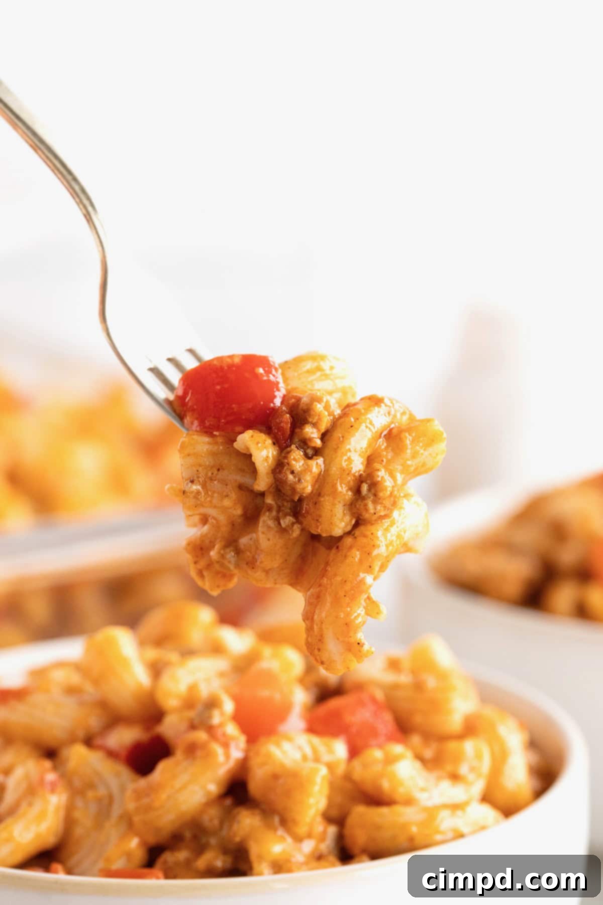 Fiesta Mac and Cheese 3 A forkful of Mexican style Mac and cheese lifted from a white bowl, showcasing the creamy texture and ingredients.