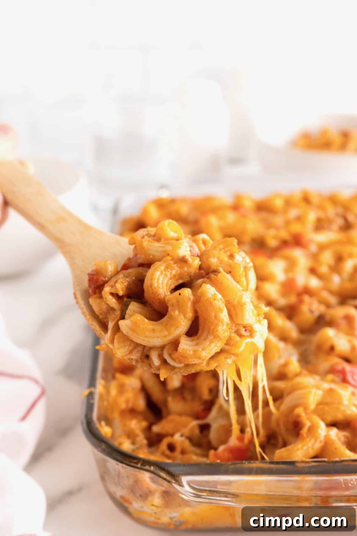Fiesta Mac and Cheese 4 A wooden spoon serving a generous portion of Mexican Mac and cheese in front of a glass casserole dish, highlighting the colorful ingredients.