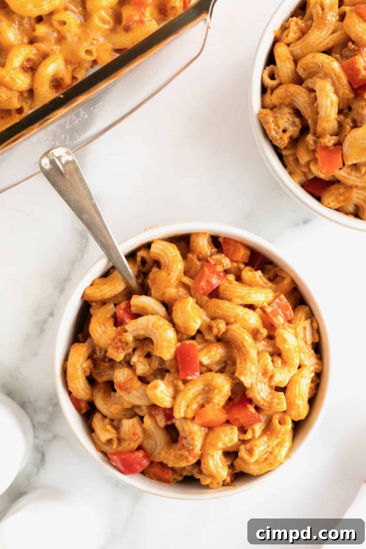 Fiesta Mac and Cheese 7 Two white bowls of Mexi Mac and Cheese with a fork to the right of the front bowl. A 9x13 glass casserole dish of the dish is visible in the background.