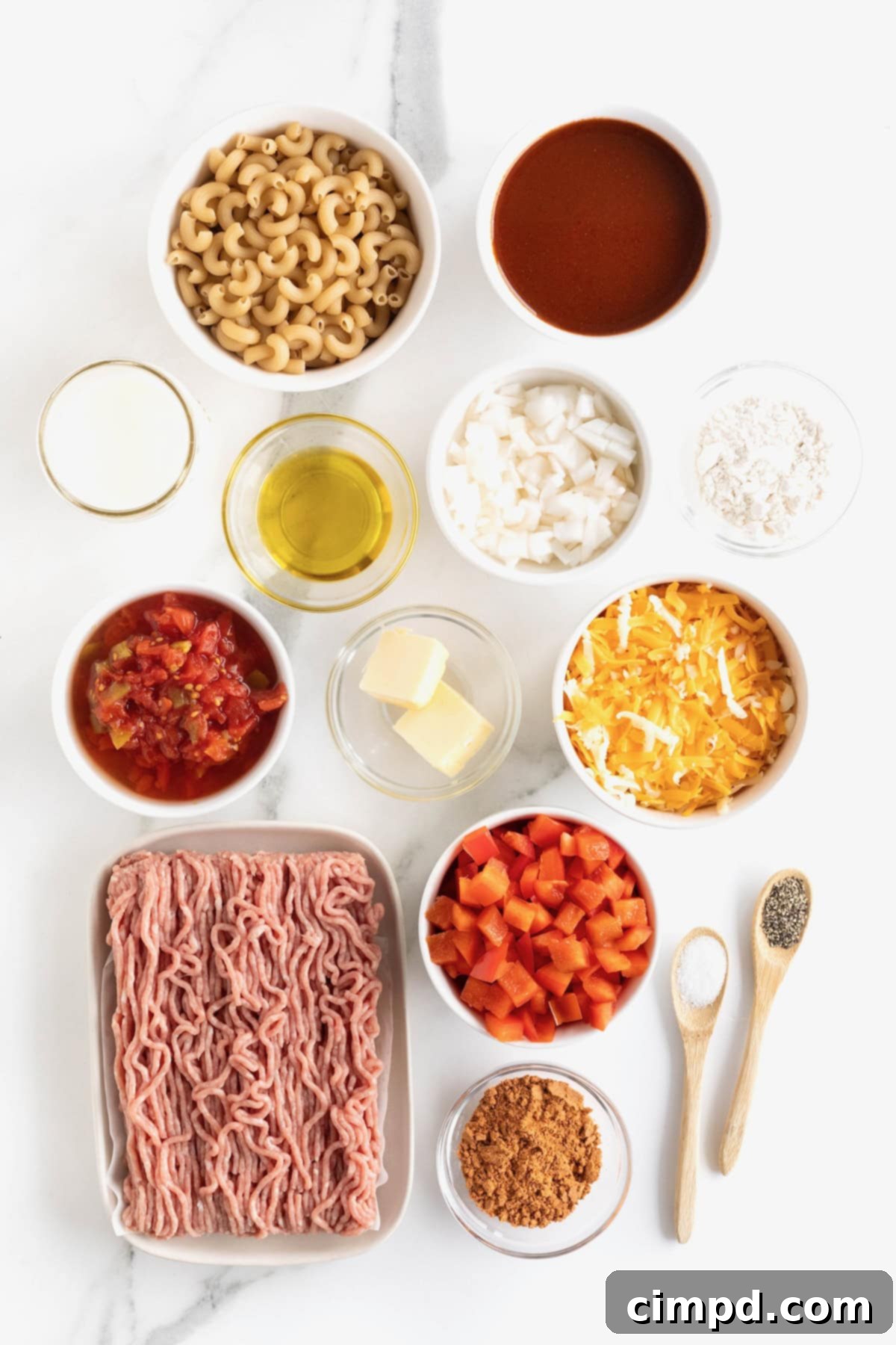 Fiesta Mac and Cheese 8 A collection of fresh ingredients for Mexi Mac and Cheese, including bell peppers, onions, cheese, and canned goods, arranged in small white dishes on a white marble counter.