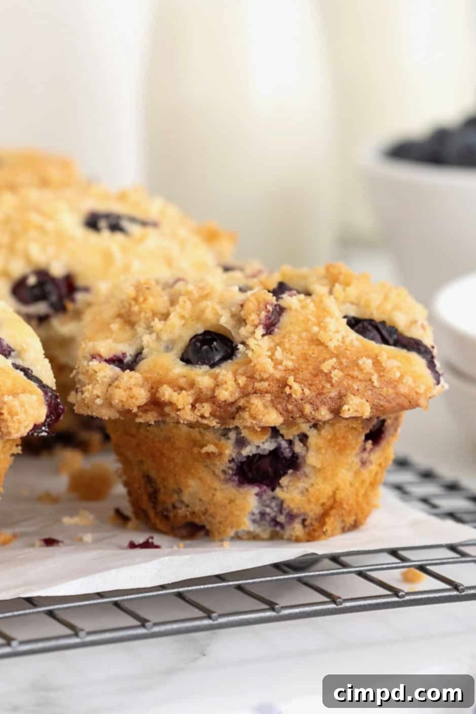 Freshly baked blueberry streusel muffins cooling on a parchment-lined wire rack, showing off their golden tops.