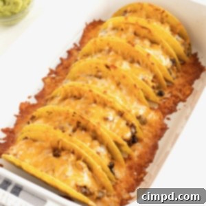 Seven tacos in a rimmed baking dish with melted cheese on top.