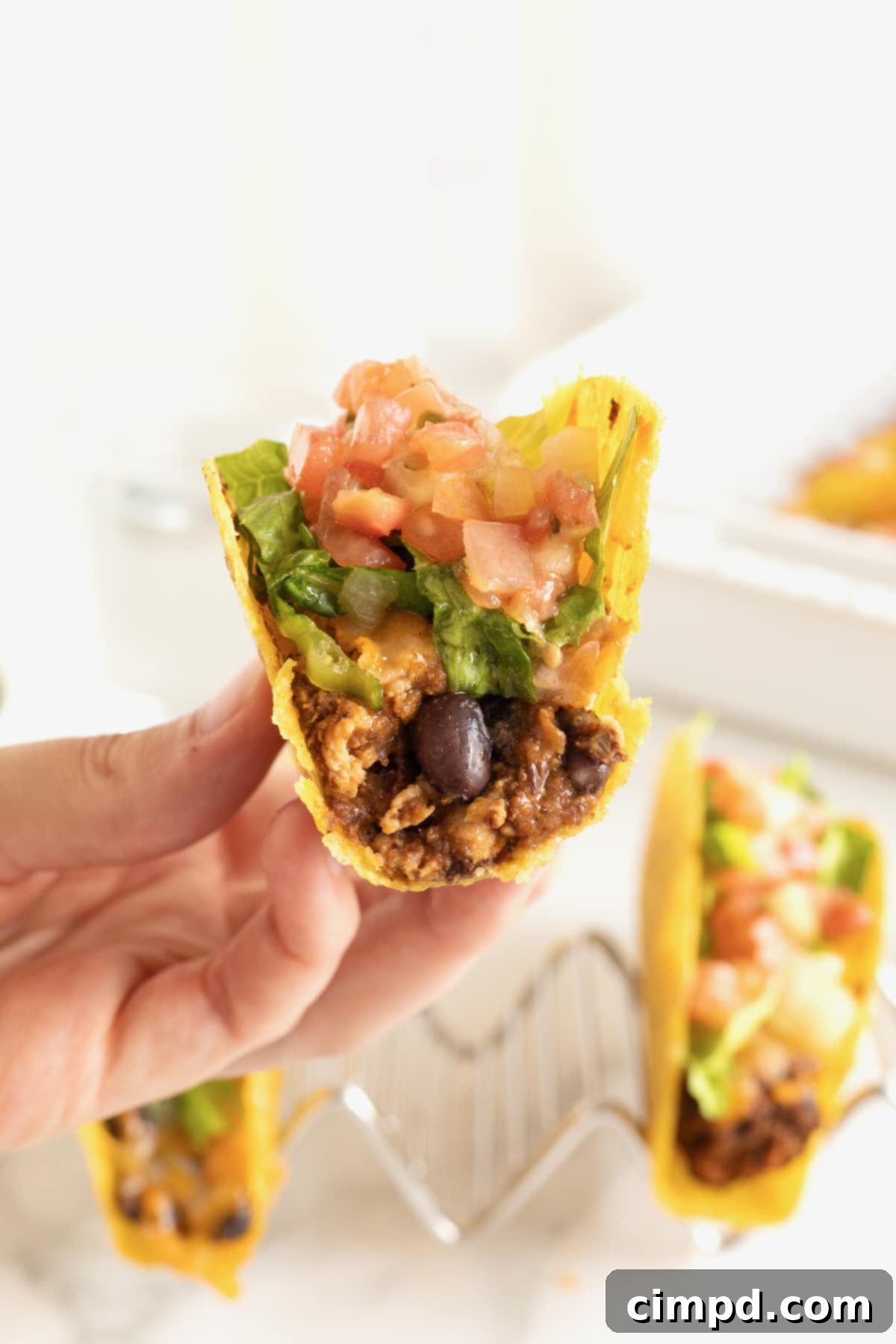 A hand holding a freshly baked turkey and black bean taco with a bite taken, showcasing the cheesy filling and crisp shell.
