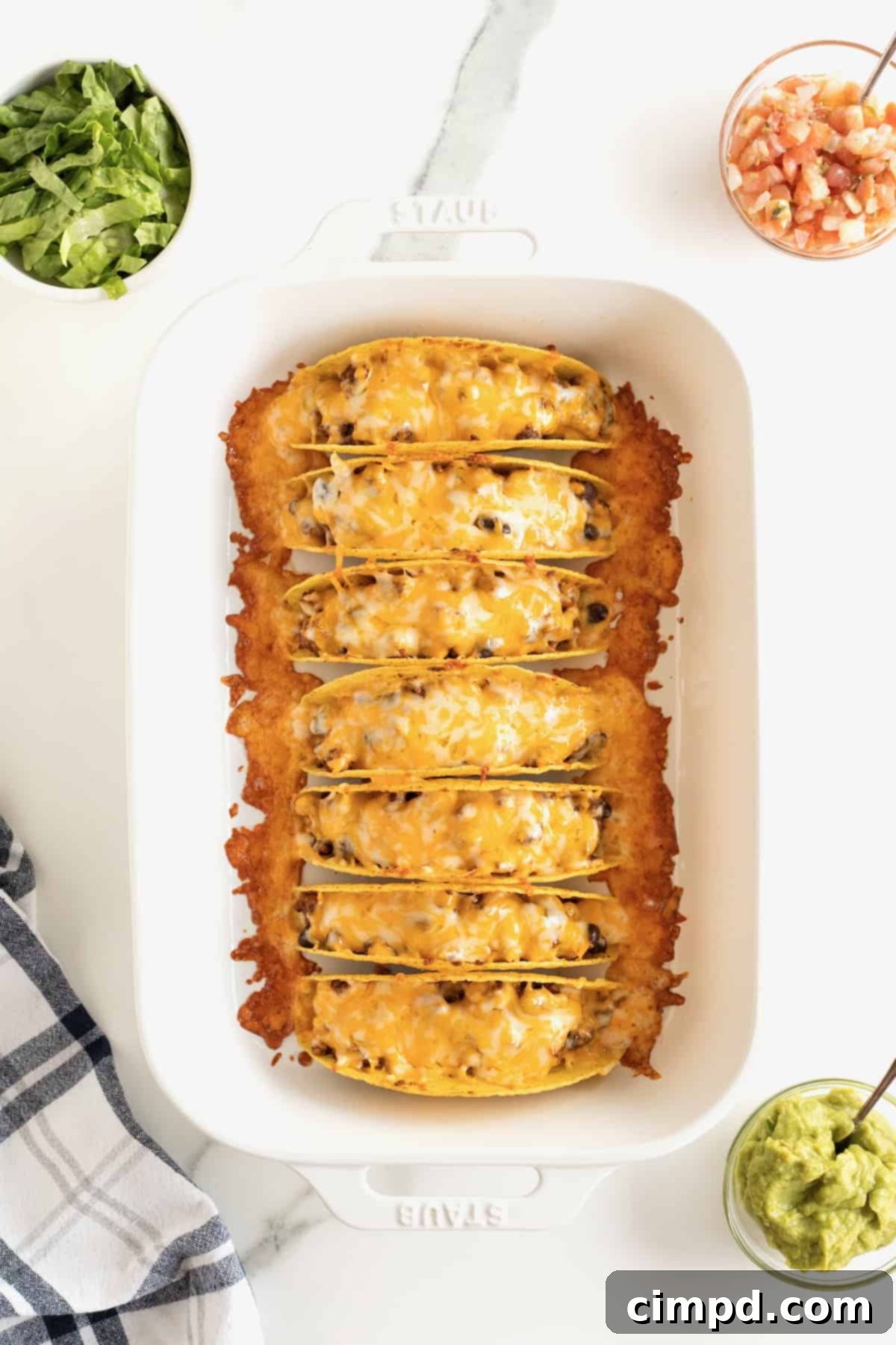 A close-up view of seven baked tacos arranged in a rimmed baking dish, garnished with perfectly melted cheese.