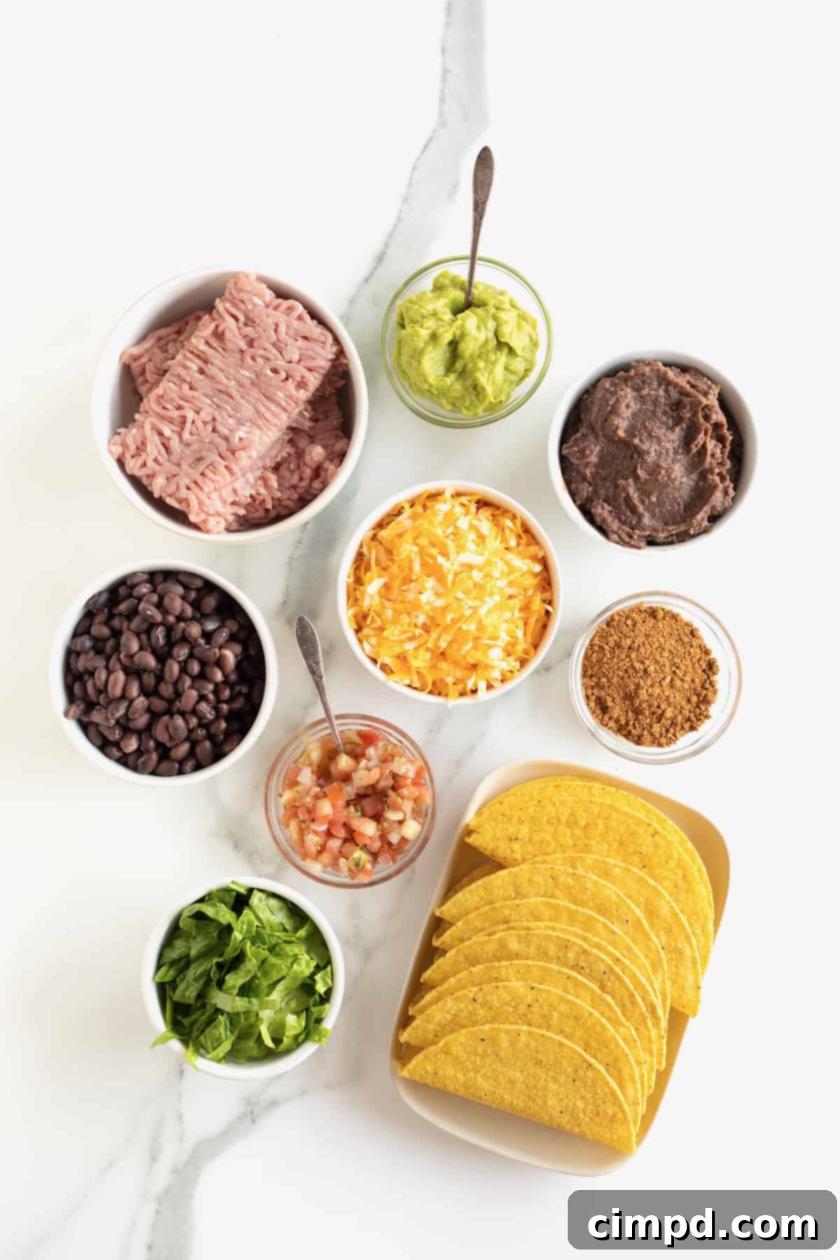 A vibrant display of fresh ingredients for turkey and black bean tacos, neatly arranged in small glass dishes on a pristine white marble counter, ready for preparation.