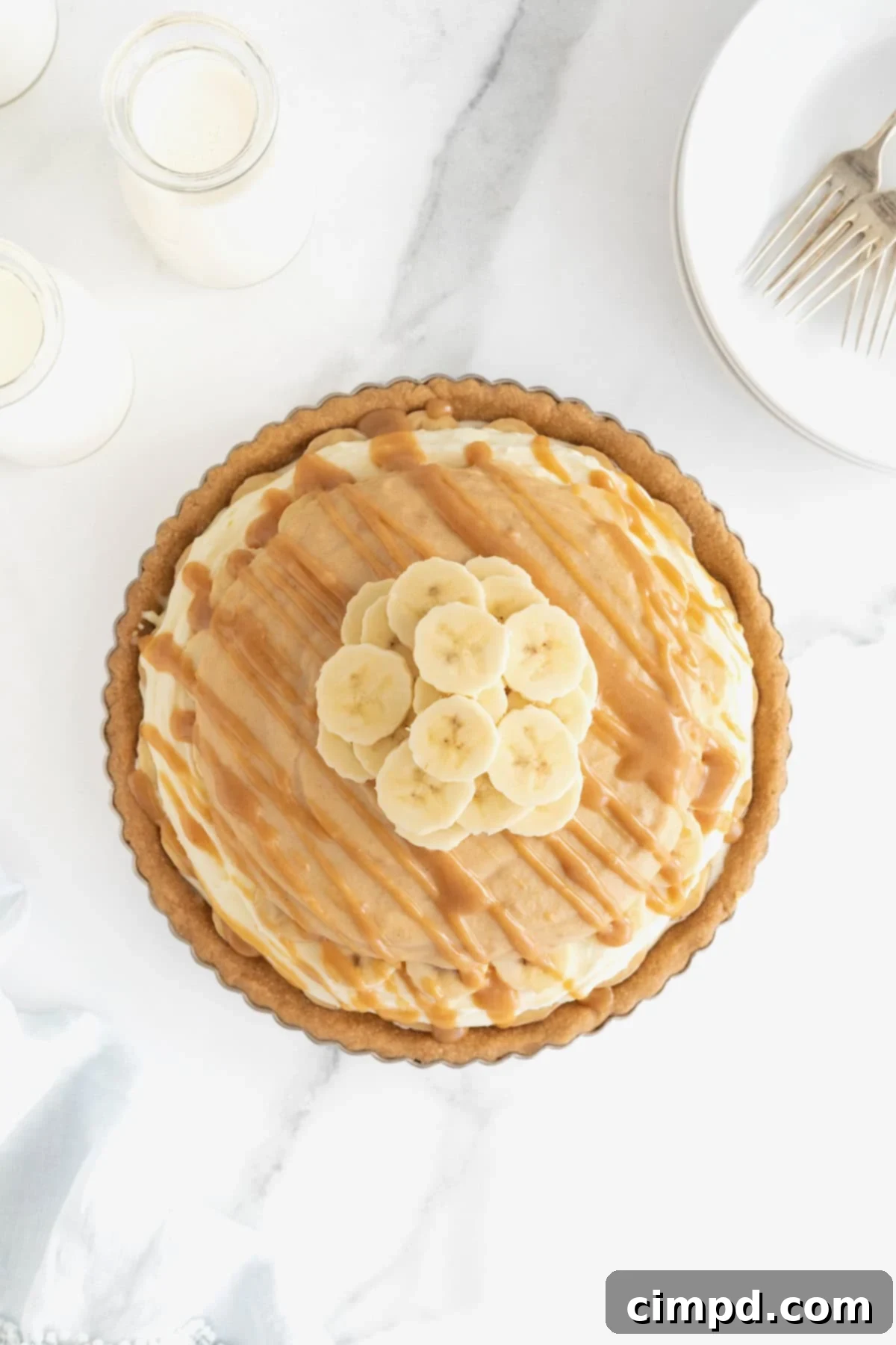 A peanut butter banana cream pie in a metal tart pan on a white marble counter.