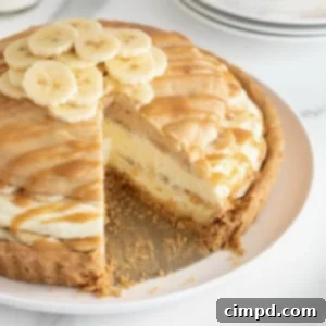 A peanut butter banana cream pie on a white cake stand. There is one slice missing from the pie.