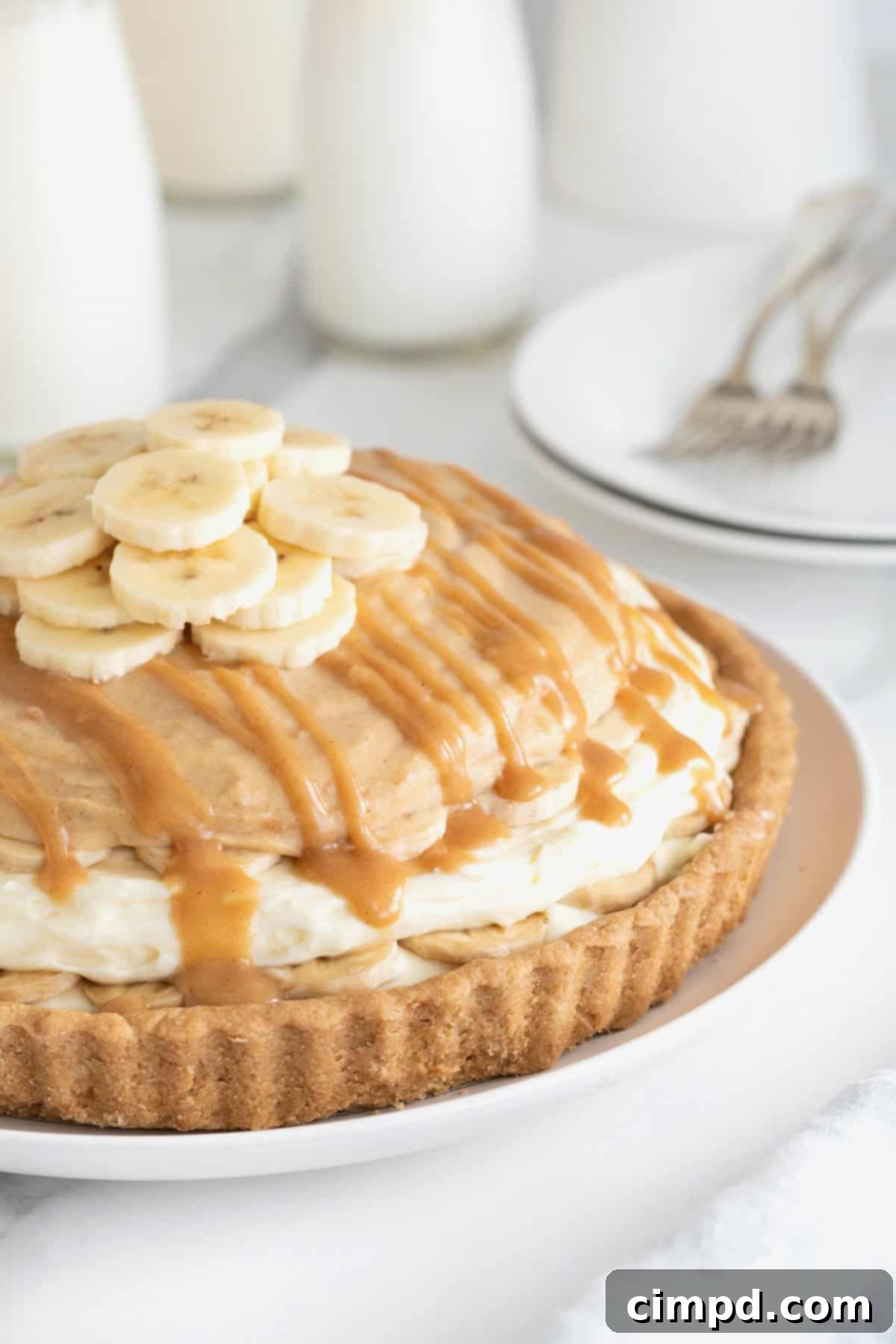 A peanut butter banana cream pie on a white cake stand on a white marble counter.