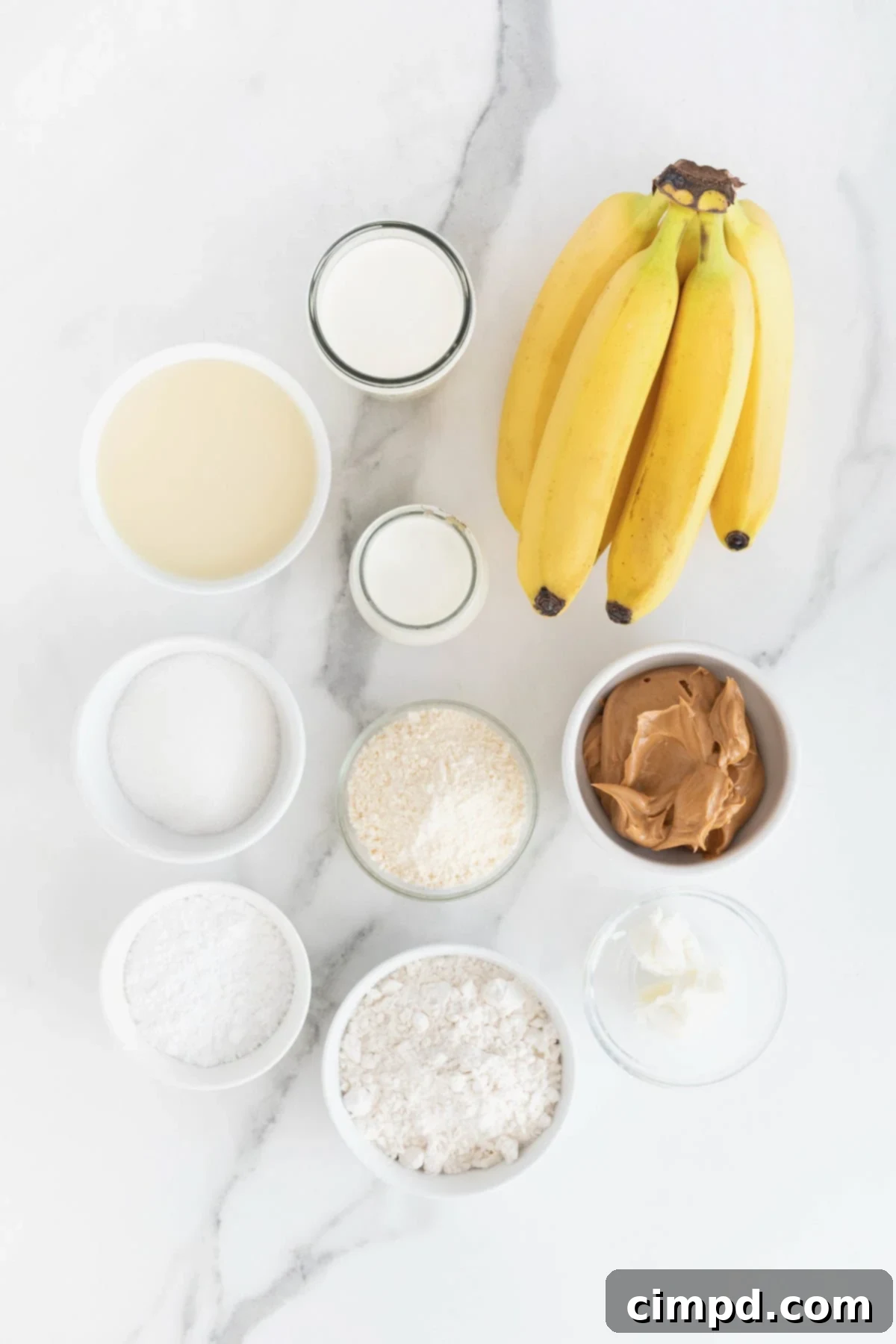 Ingredients to make a peanut butter banana cream pie in small white dishes on a white marble counter.