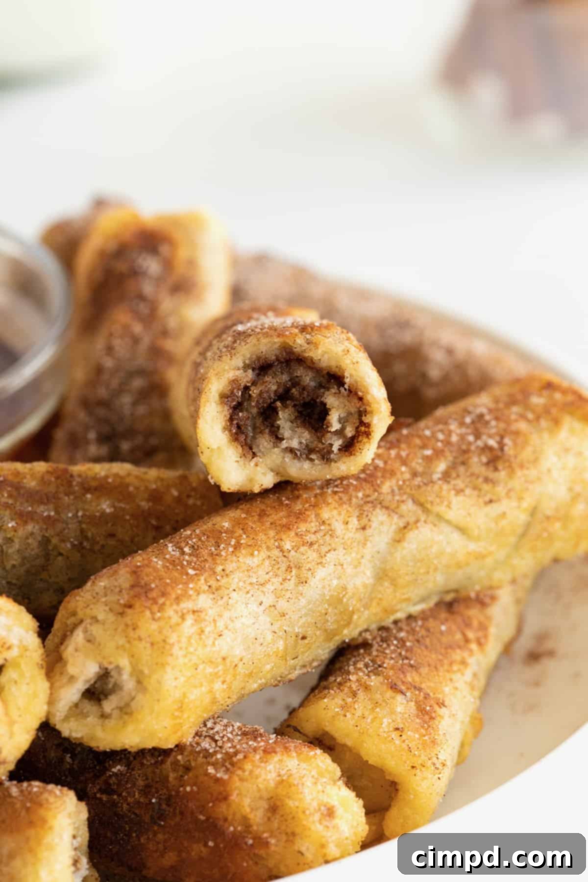A perfectly arranged stack of golden-brown French toast roll-ups sits on a pristine white plate, ready to be enjoyed.