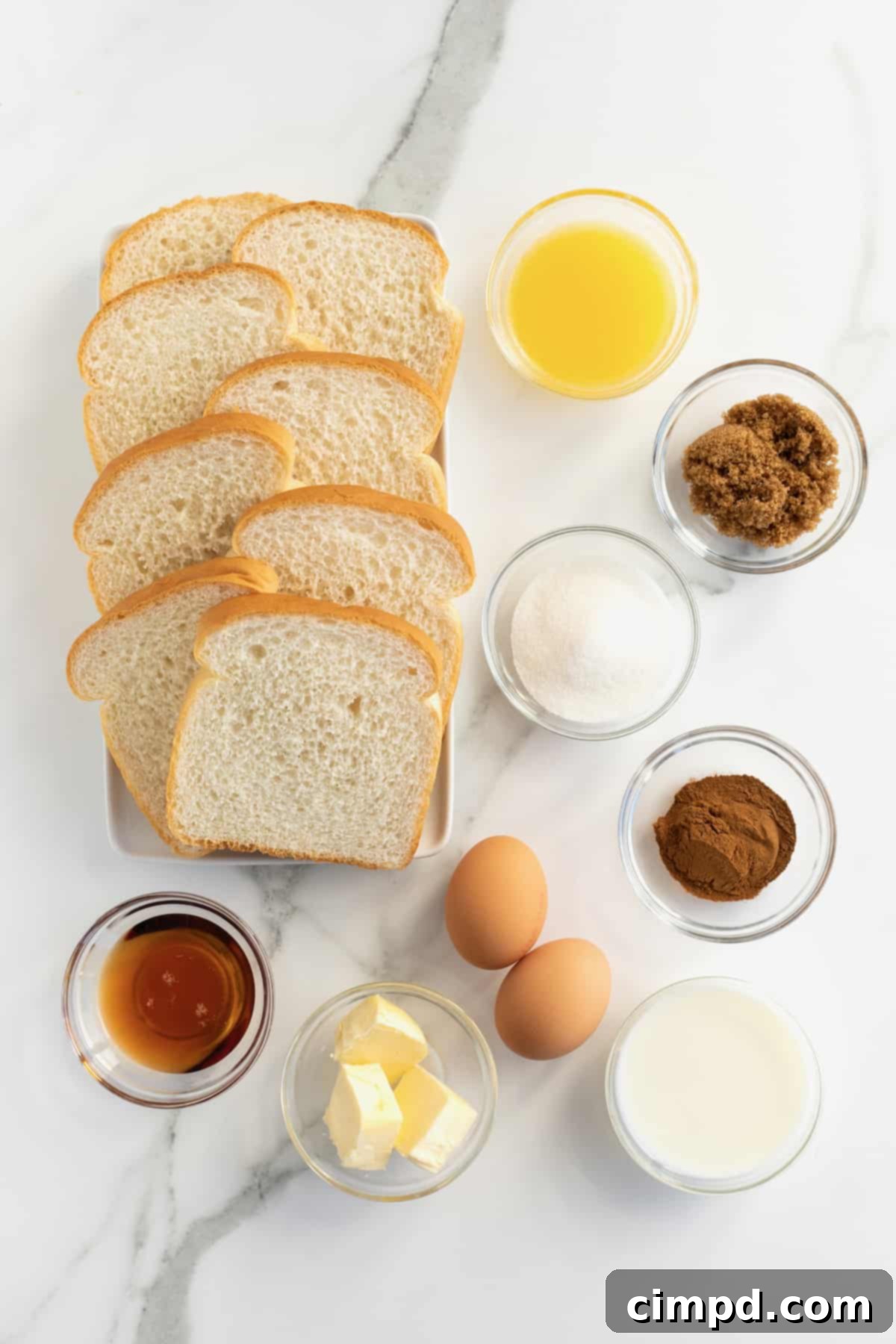 A kitchen counter displays neatly sliced white bread, fresh brown eggs, and elegant glass dishes containing essential ingredients: warm maple syrup, fragrant cinnamon, granular sugar, and shimmering melted butter.