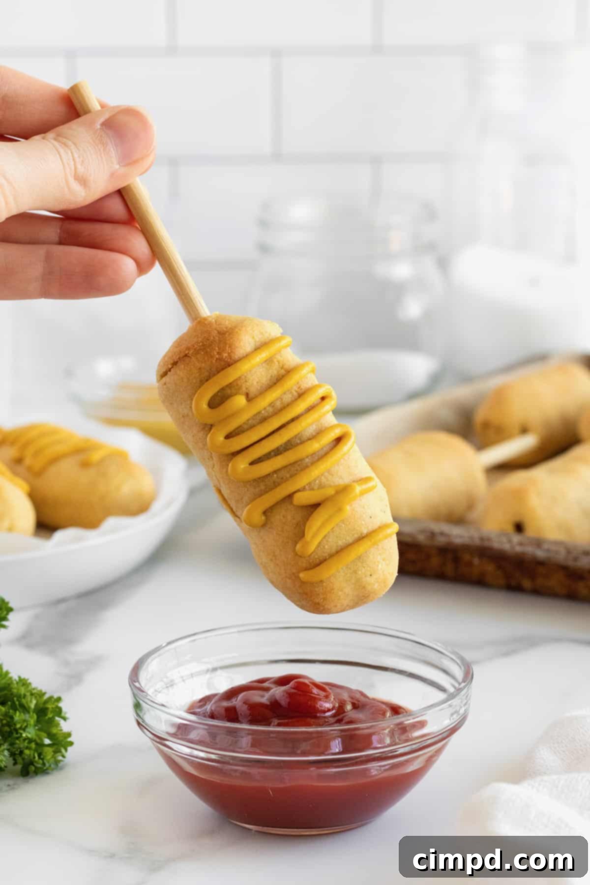 A close-up shot of a plate of baked corn dogs with dipping sauces, showcasing their golden crust and perfect presentation.