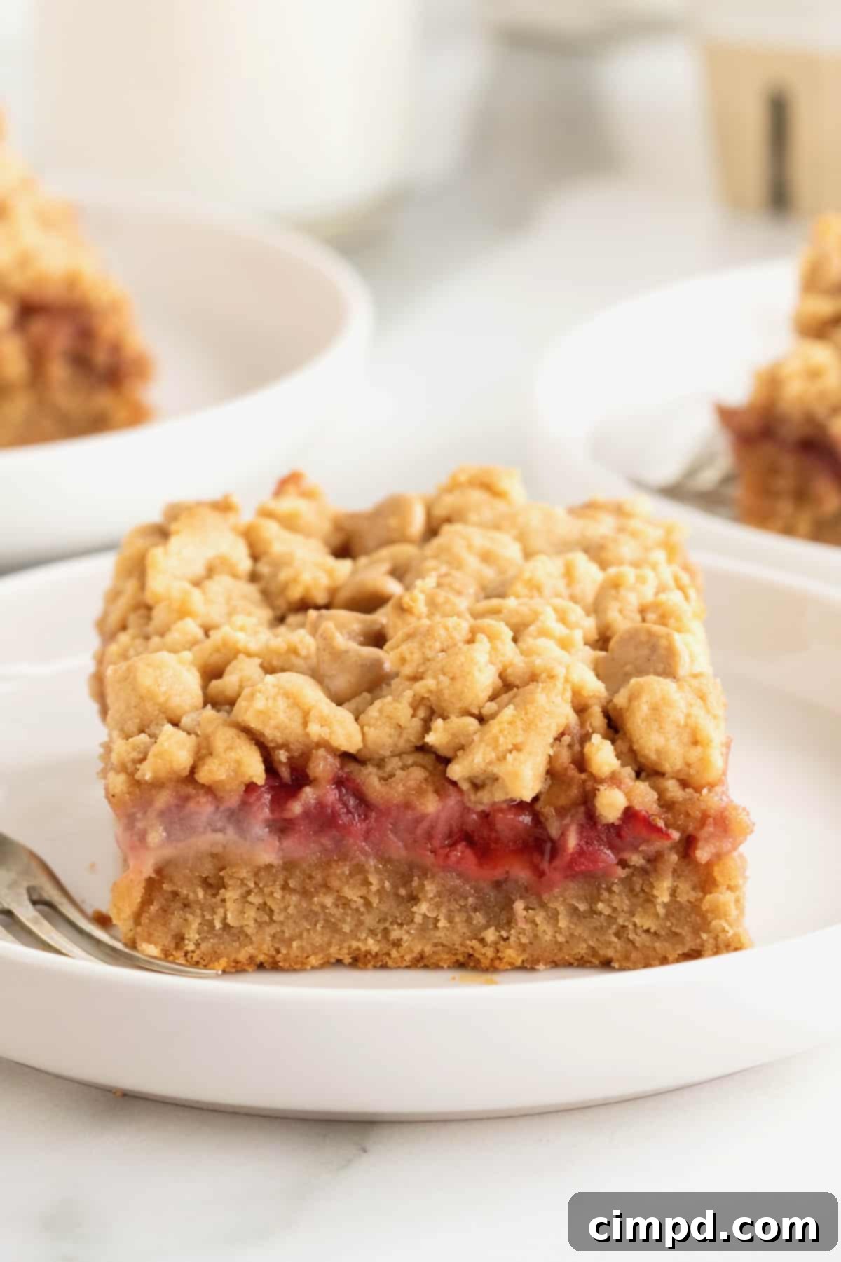 Strawberry Peanut Butter Swirl Bars 2 A single strawberry peanut butter bar resting on a white rimmed plate with a silver fork beside it, ready to be enjoyed.