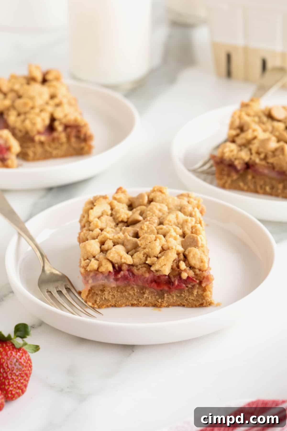 Strawberry Peanut Butter Swirl Bars 4 Three strawberry peanut butter bars displayed on white rimmed plates, with a fork on the front plate, inviting a taste.