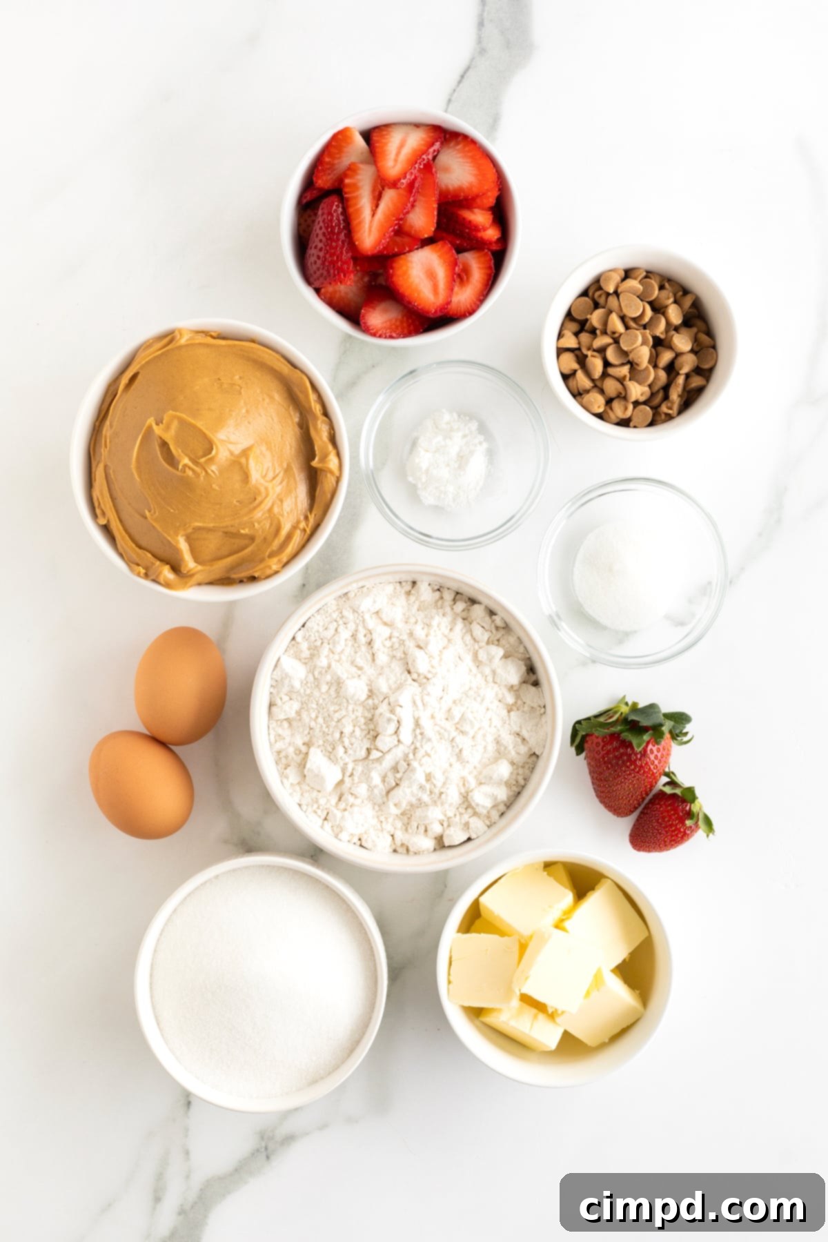 Strawberry Peanut Butter Swirl Bars 7 Various ingredients for strawberry peanut butter bars, including butter, sugar, eggs, peanut butter, flour, salt, baking powder, and strawberries, arranged in small glass dishes on a white marble counter.
