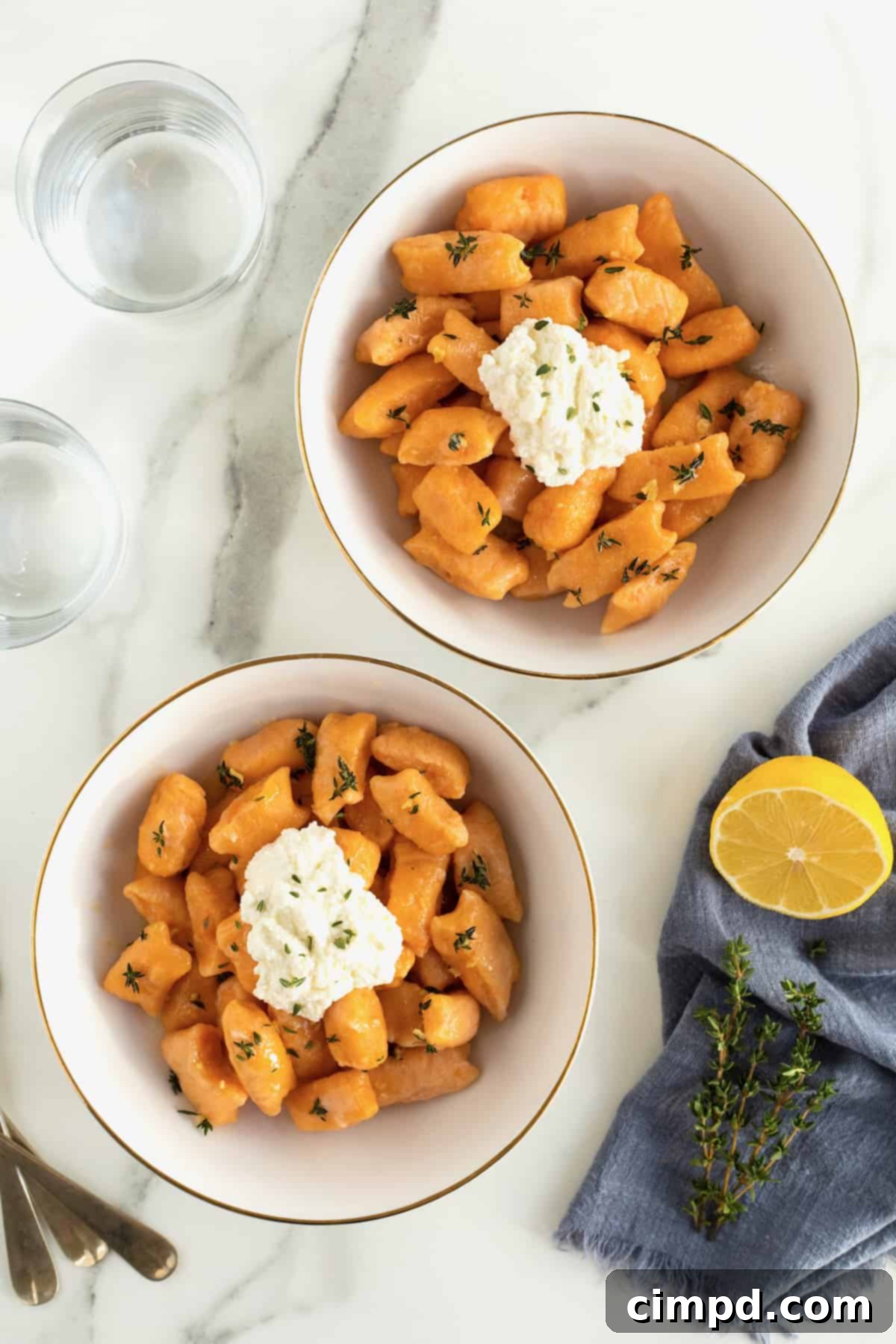 Two gold-rimmed white bowls, each filled with delicious sweet potato gnocchi and topped with fresh ricotta, presented beautifully.