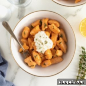 A gold-rimmed white bowl of sweet potato gnocchi with a dollop of fresh ricotta on top.