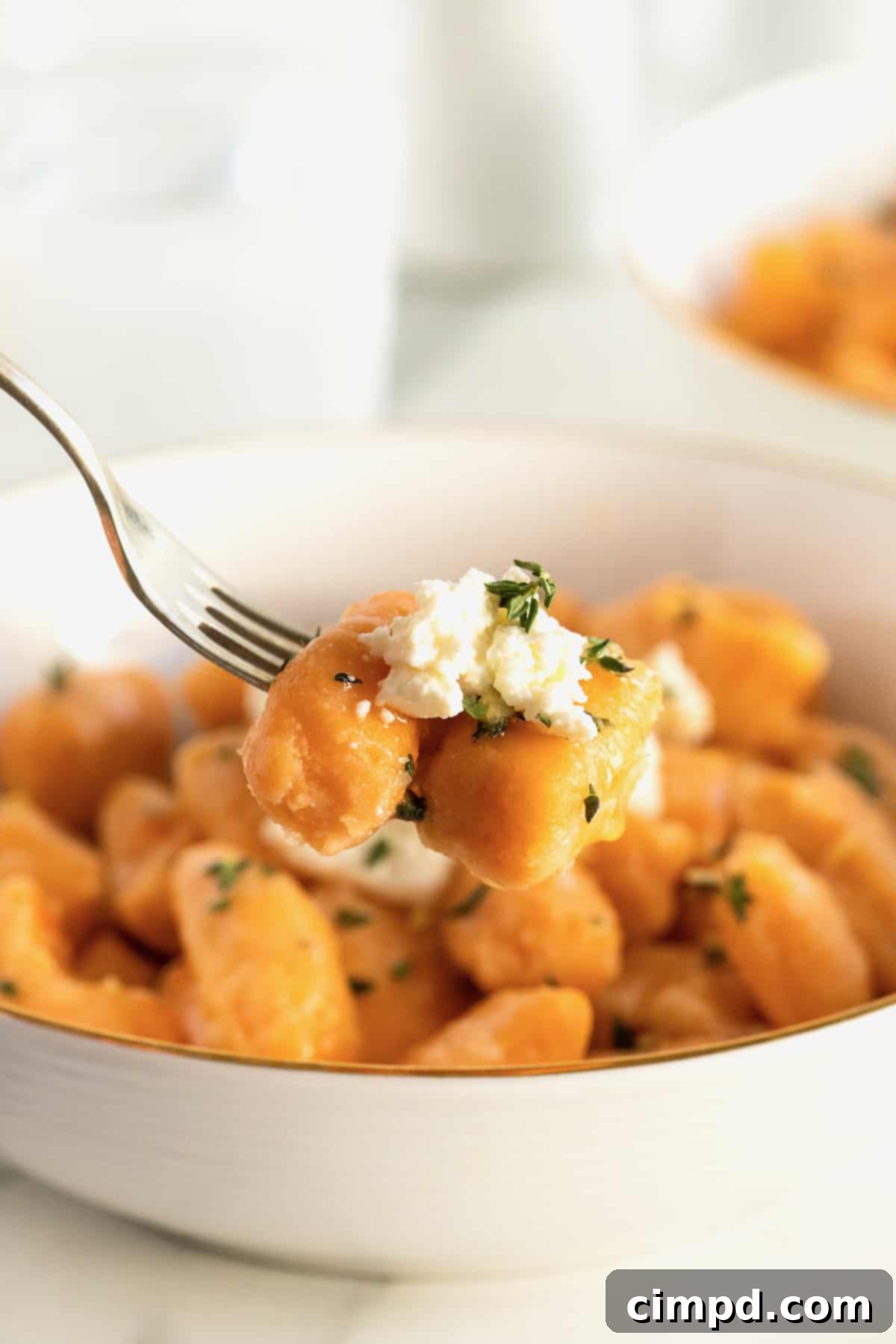 A close-up shot of a fork lifting a piece of sweet potato gnocchi, revealing its soft texture, adorned with ricotta and sauce.