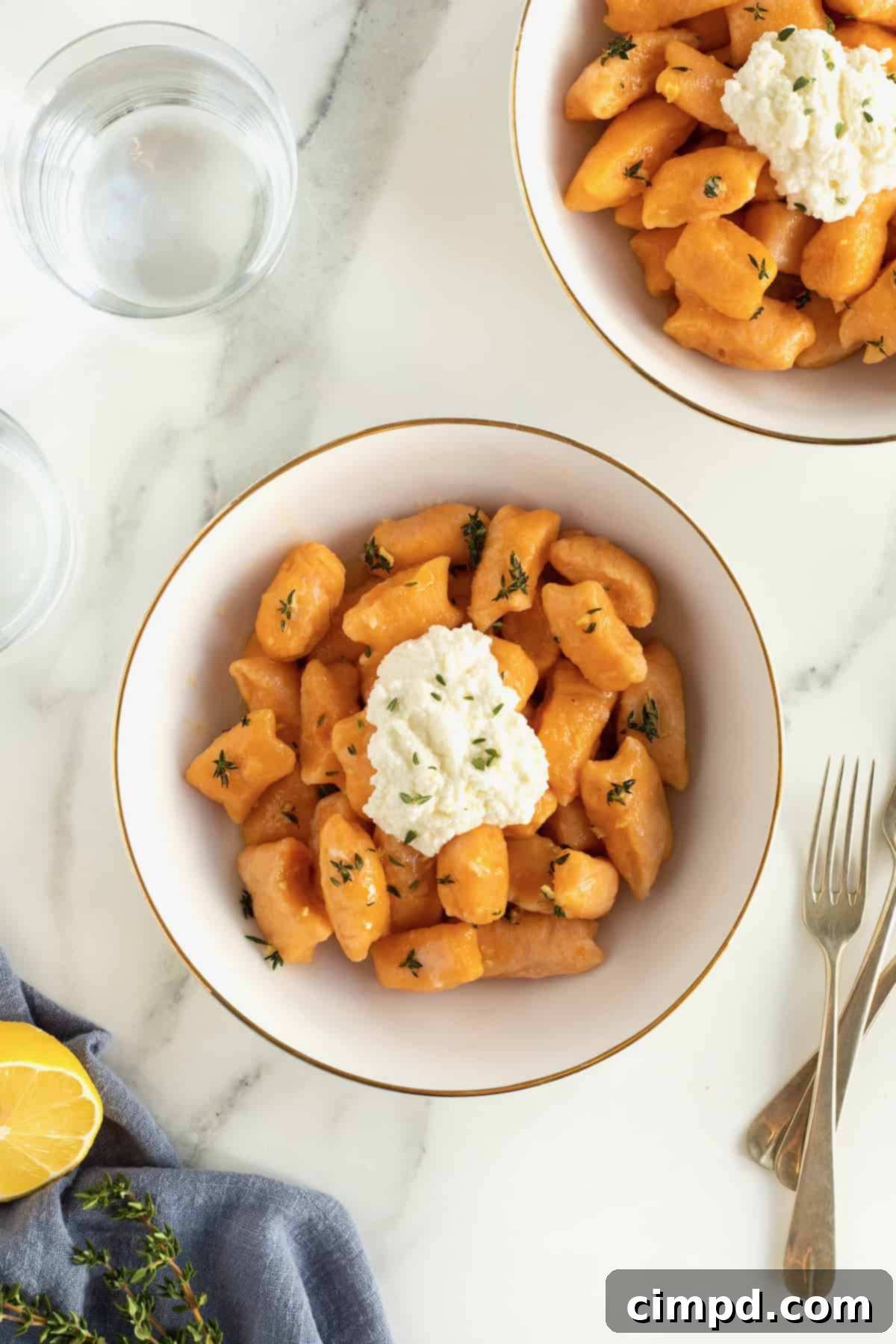A beautifully arranged gold-rimmed white bowl filled with sweet potato gnocchi, garnished with a generous dollop of creamy ricotta.