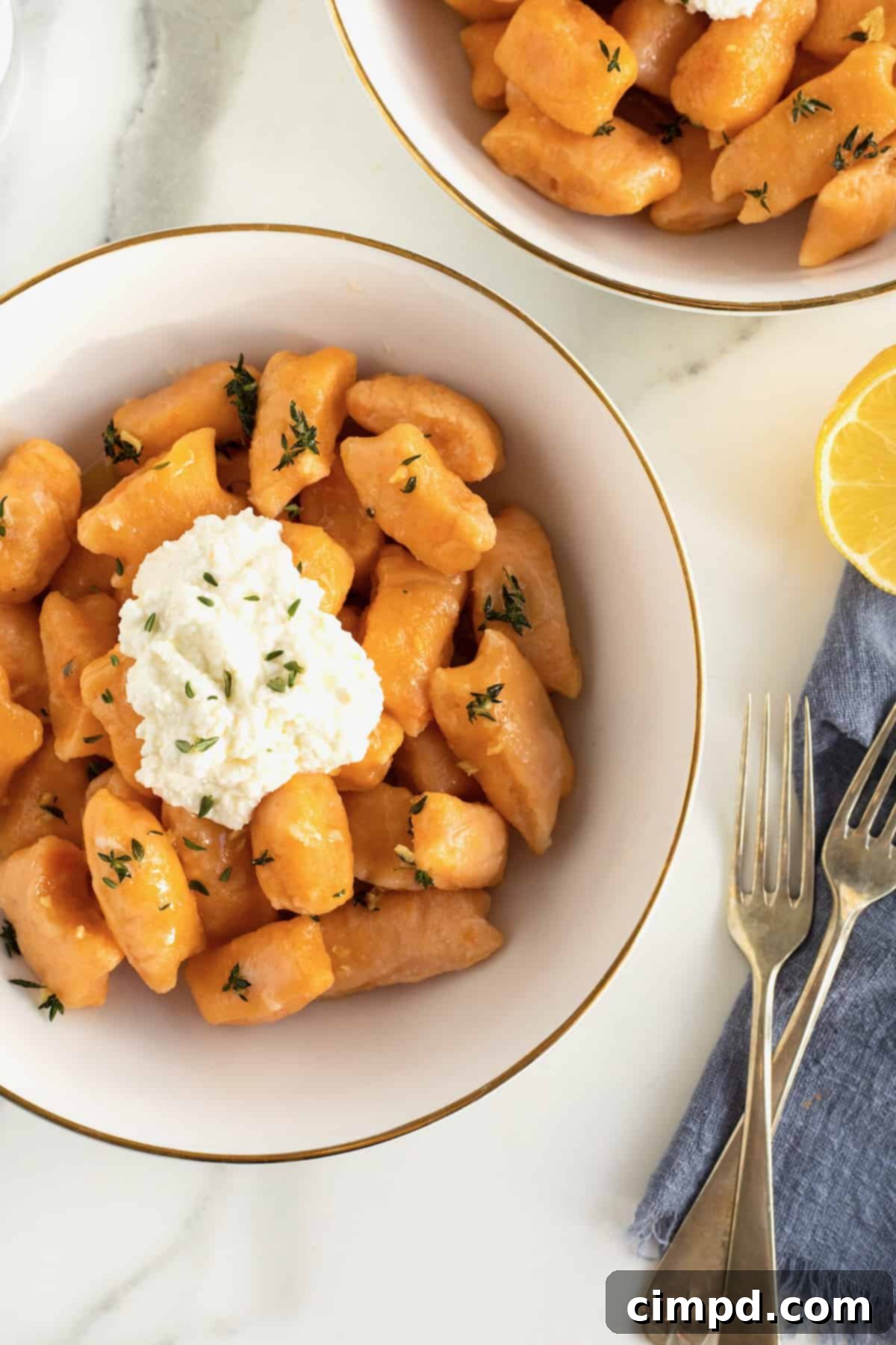 A captivating overhead shot of a white bowl with a golden rim, holding a serving of sweet potato gnocchi, topped with fluffy ricotta.