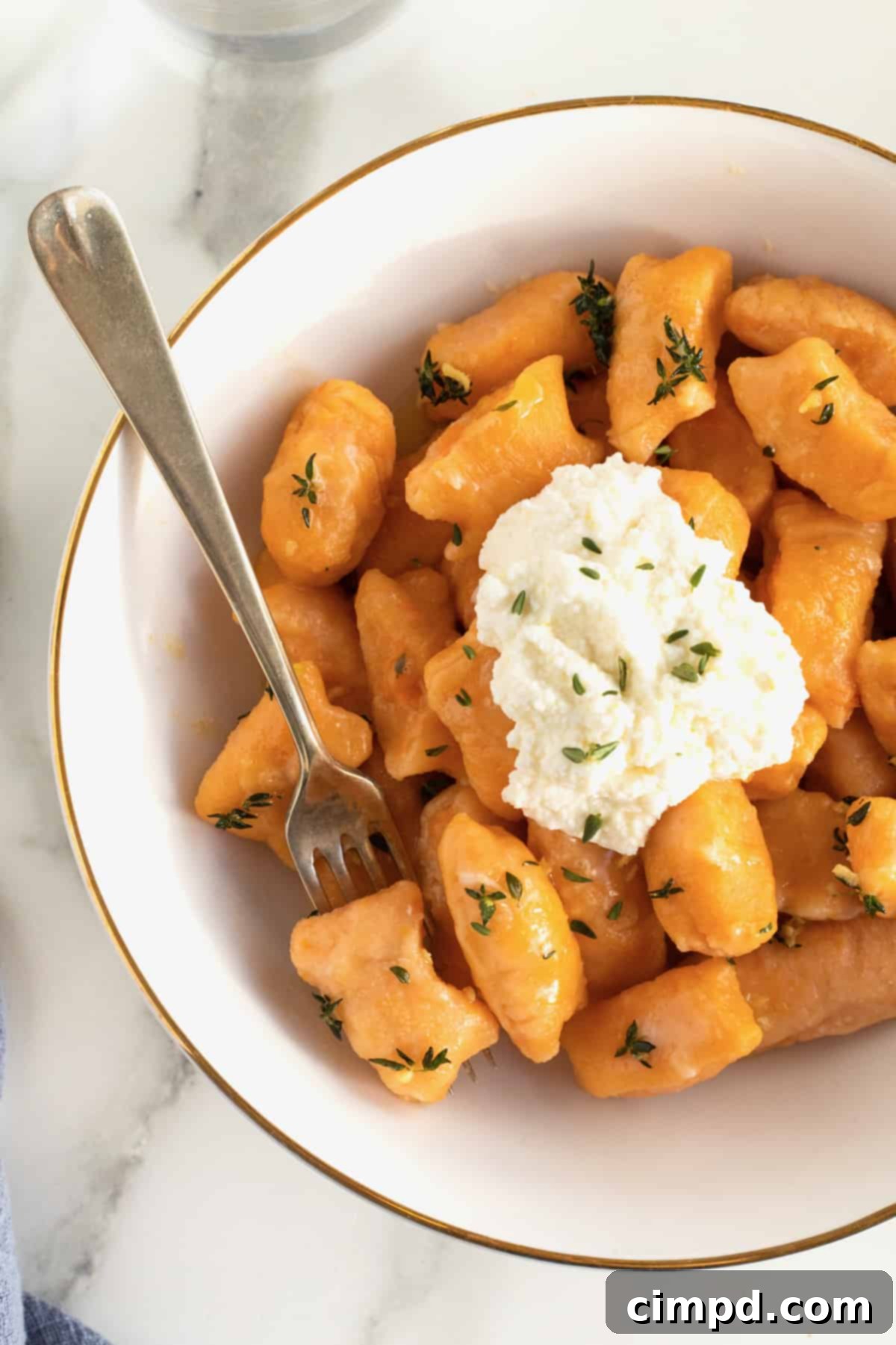Another enticing view of a gold-rimmed white bowl filled with sweet potato gnocchi, crowned with a pristine dollop of fresh ricotta.