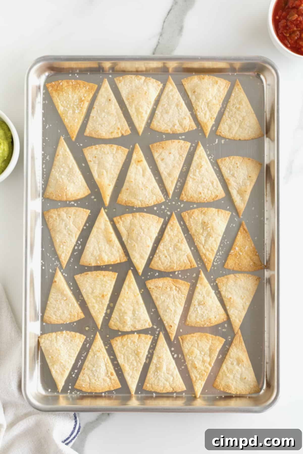 A baking sheet filled with a fresh batch of golden-brown, crispy homemade baked tortilla chips, straight from the oven.