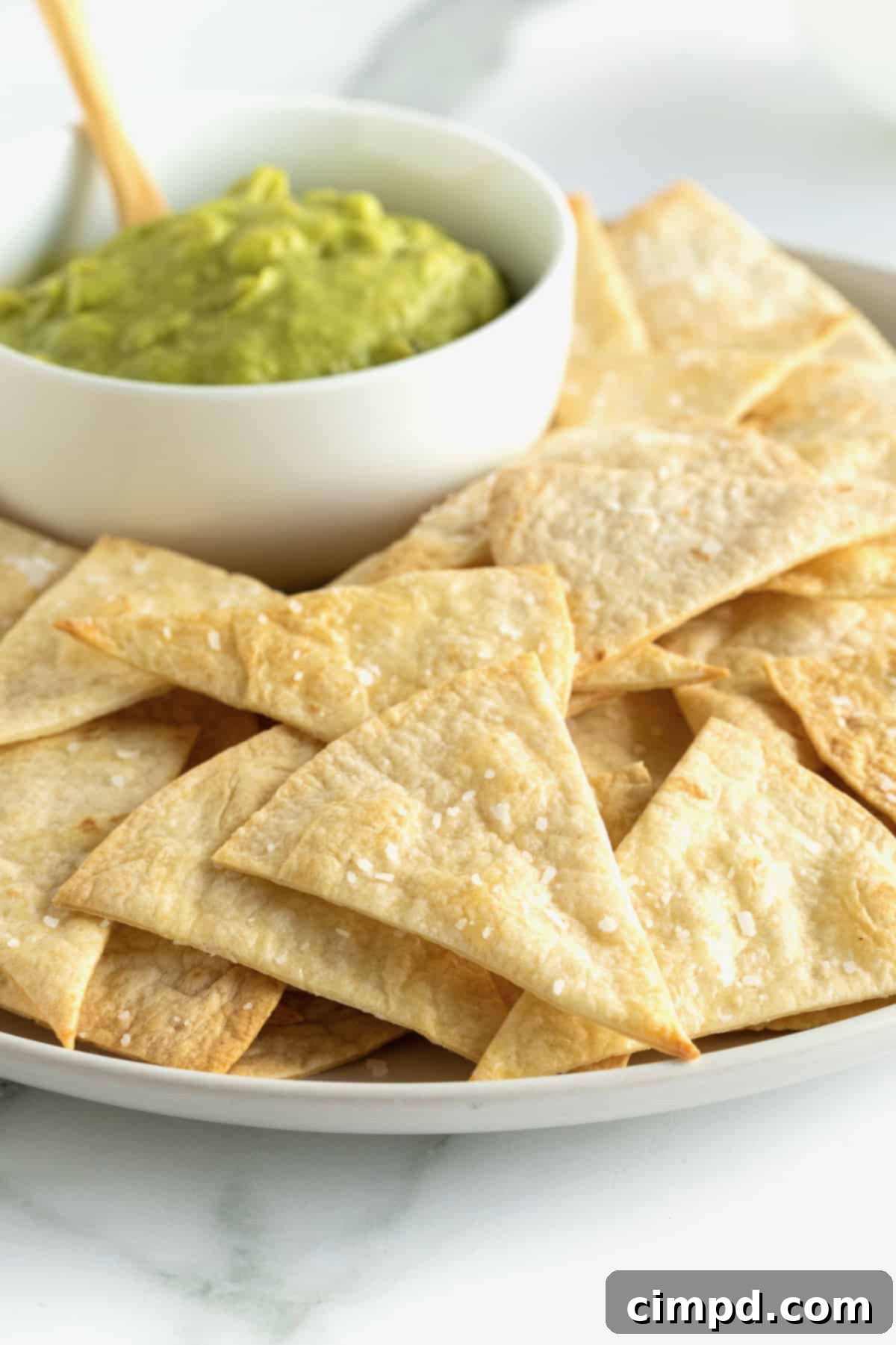 A beautifully arranged plate of homemade baked flour tortilla chips, accompanied by a rich bowl of guacamole, ready for dipping.